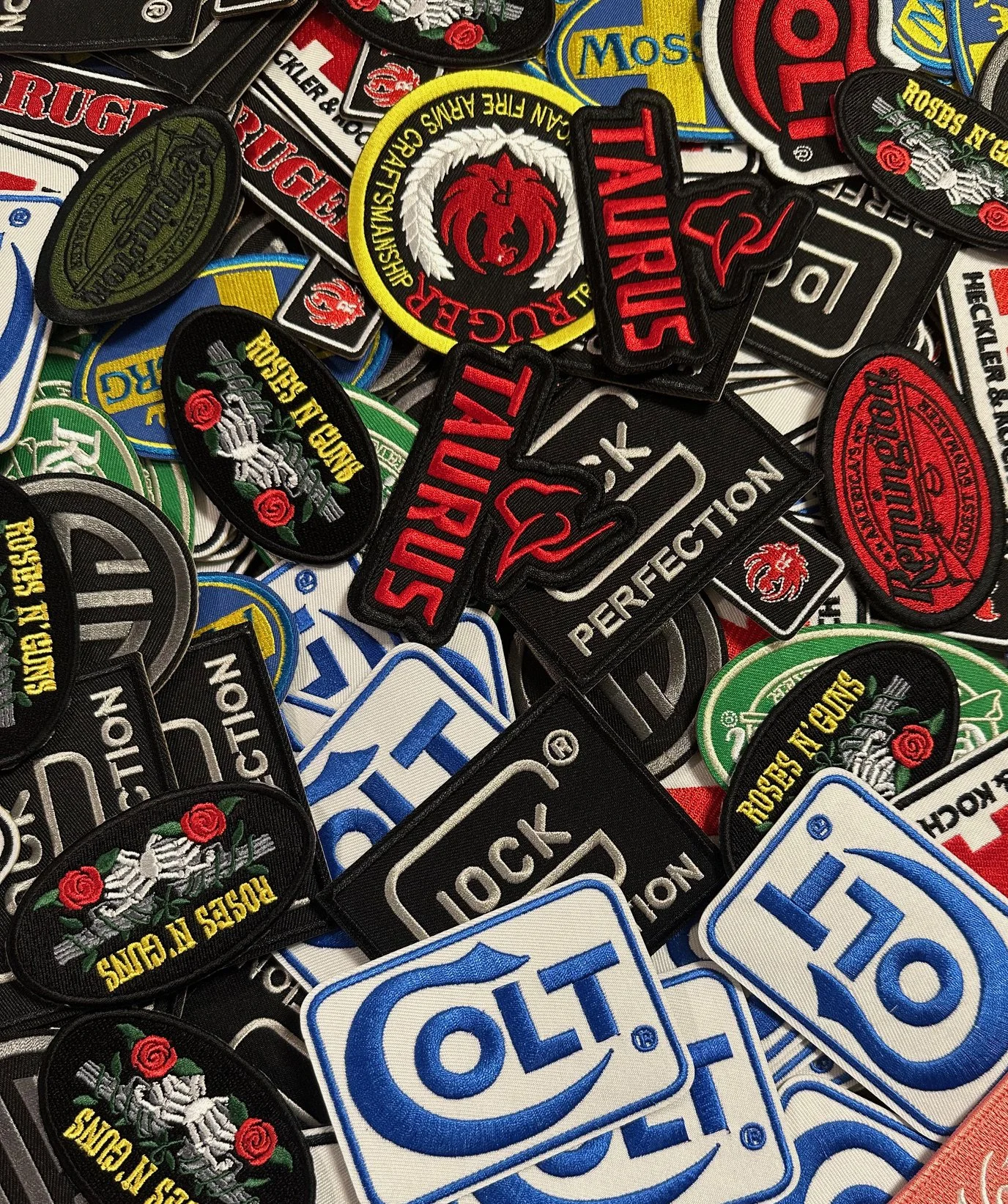 A collection of embroidered patches from various brands, including logos and symbols, mostly related to firearm and gun culture.