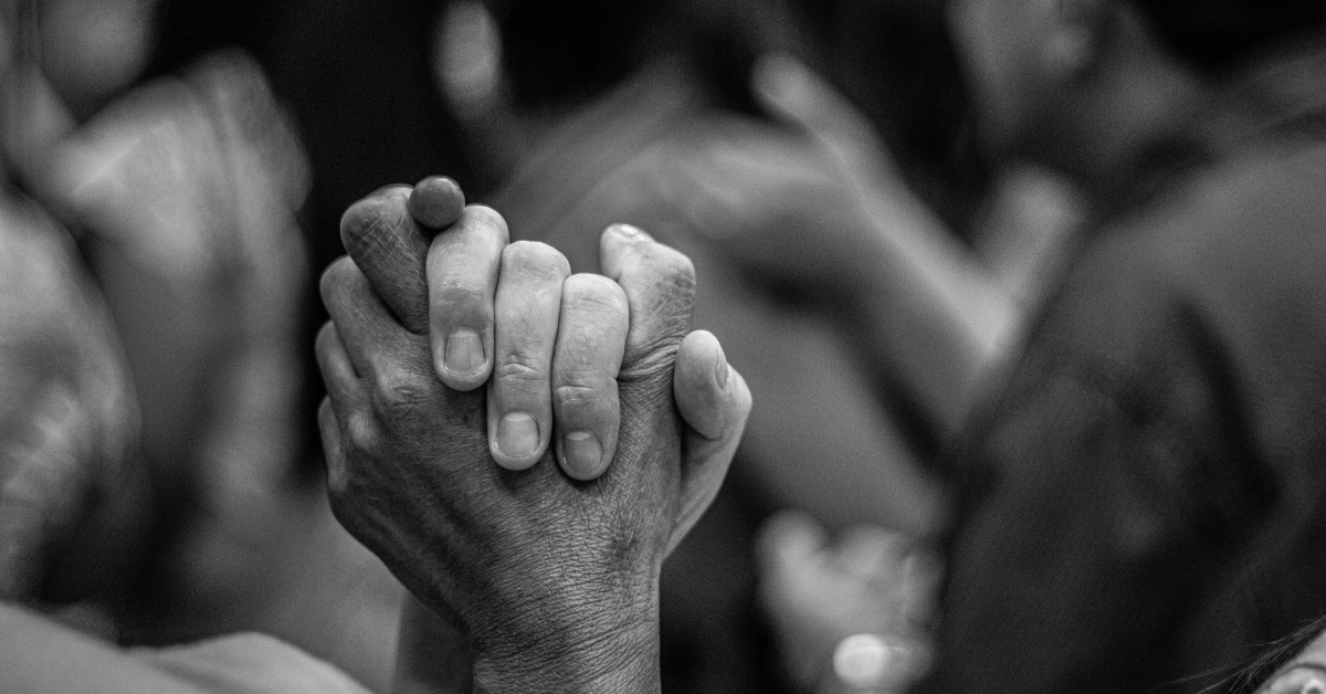 Close-up of two people holding hands in prayer or a moment of connection.