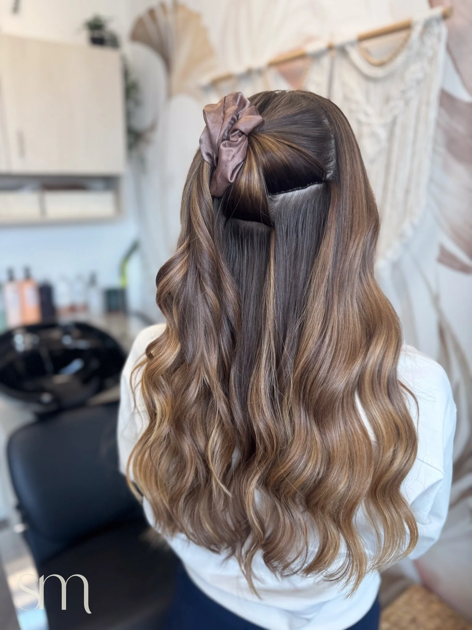Back of a woman's head with long, wavy, ombre brown hair styled with sections clipped back and a satin scrunchie accessory.