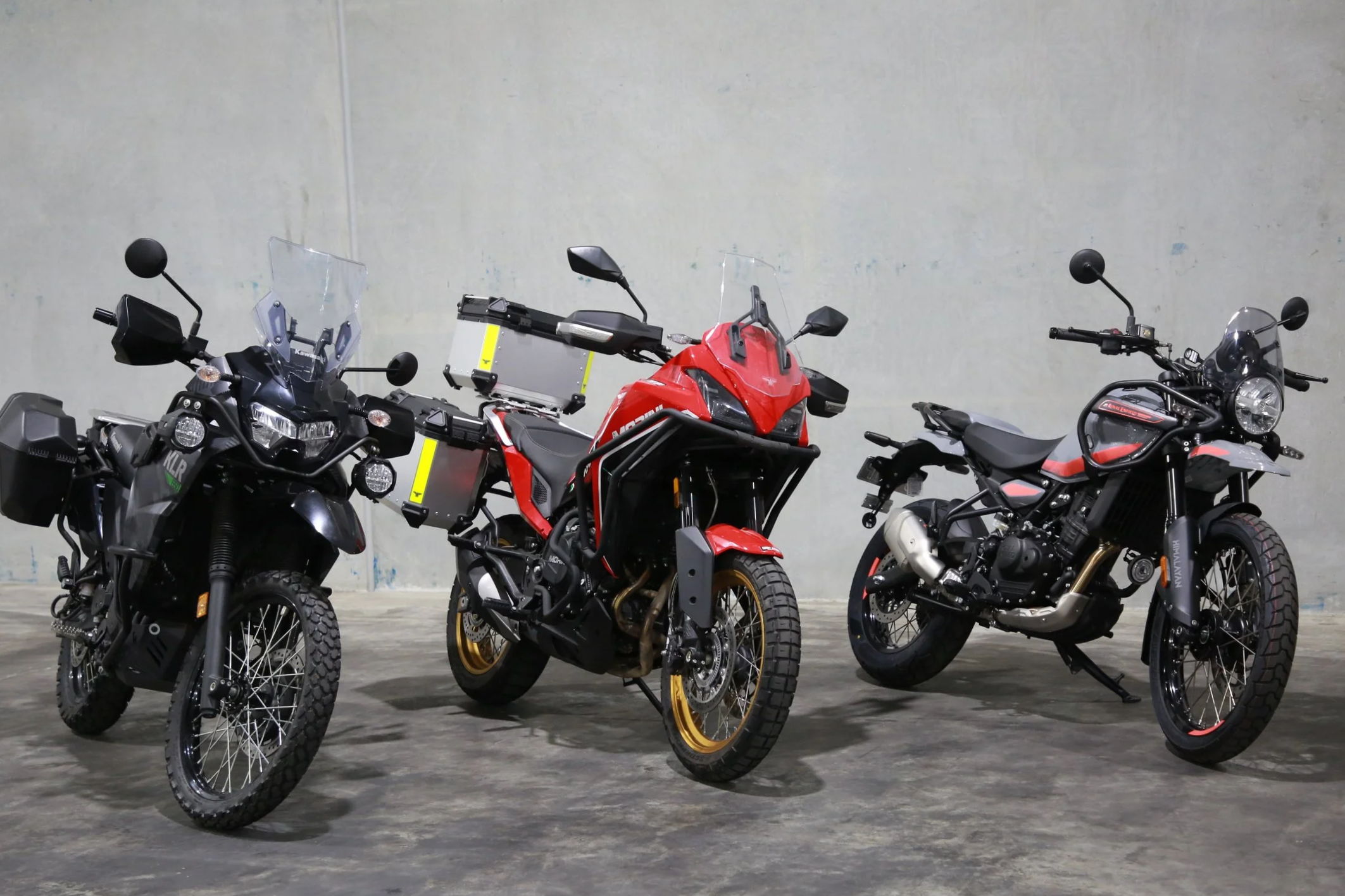 Three adventure and touring motorcycles parked indoors against a plain wall.