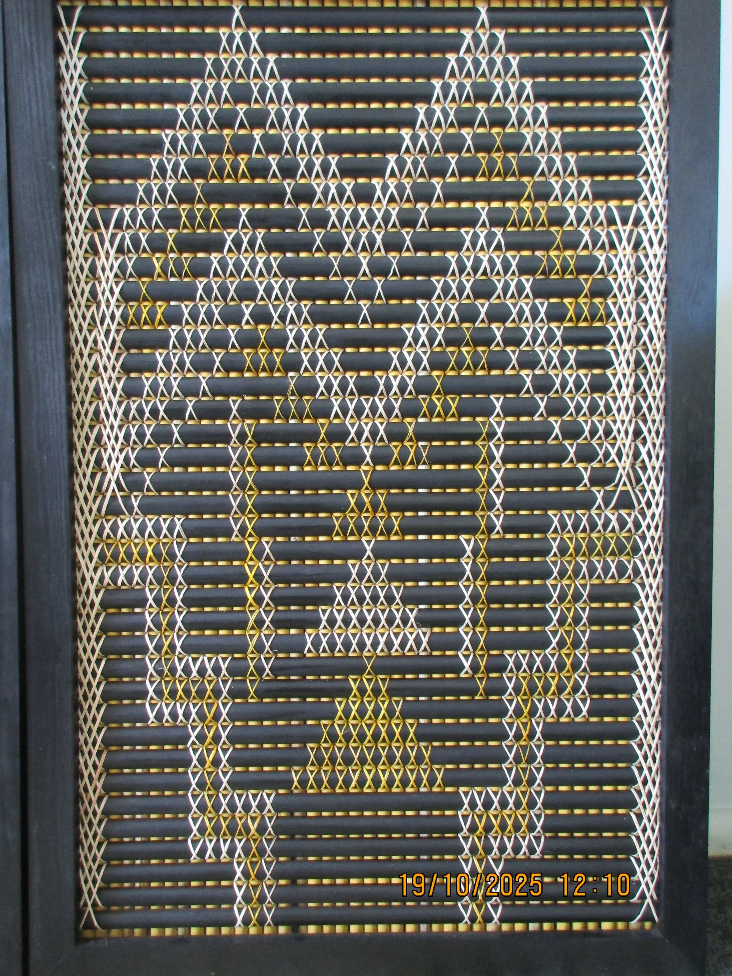 Decorative wooden panel with intricate geometric star-shaped pattern in white and yellow, framed by a black border.