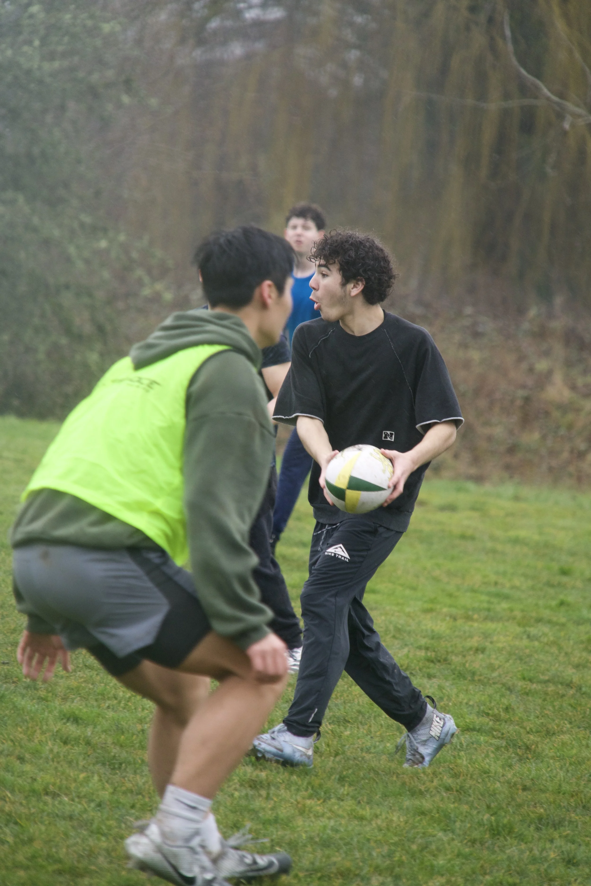 Group of young people playing rugby outdoors on a grassy field.