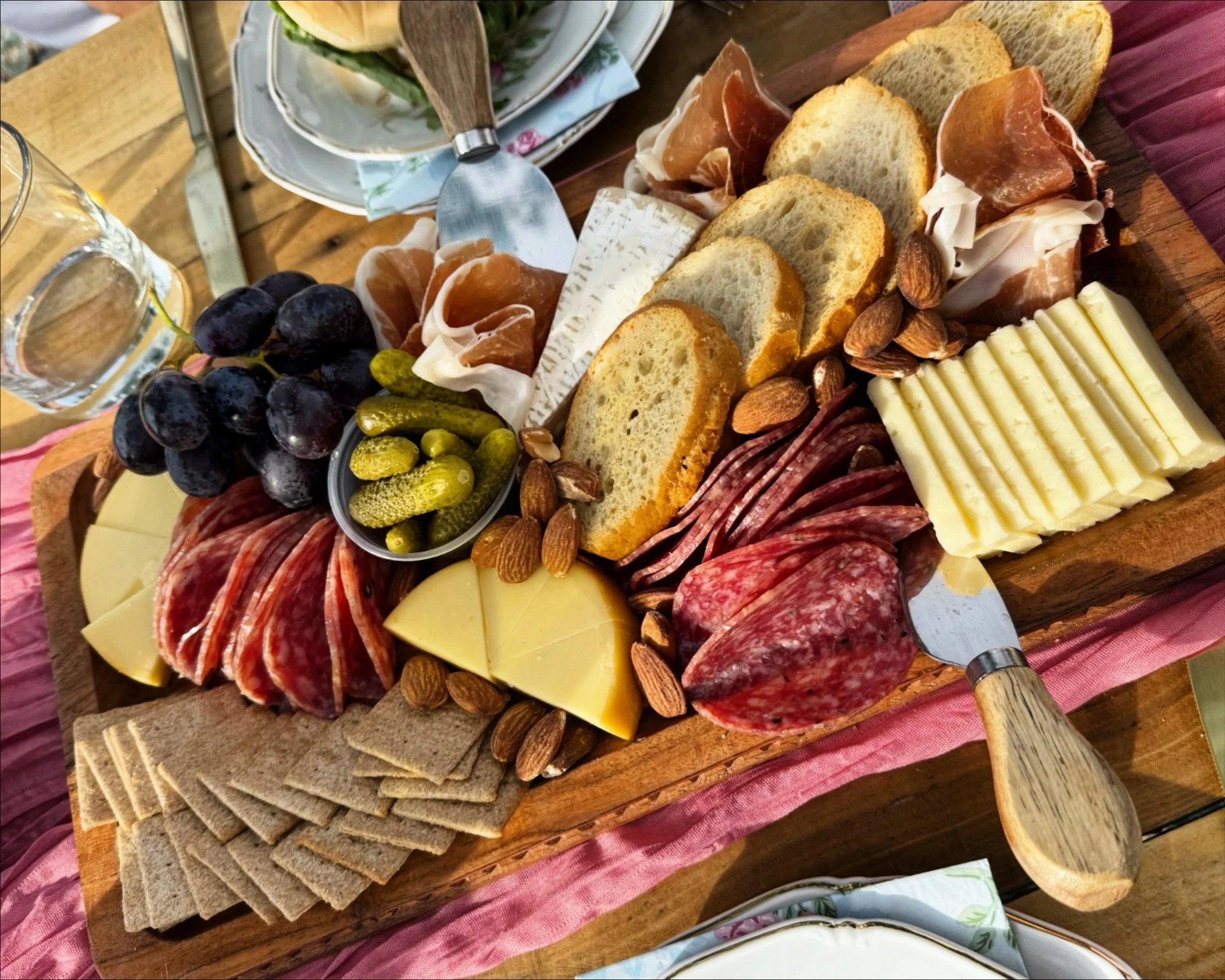 Charcuterie board with assorted meats, crackers, cheeses, fruits like blueberries and pomegranate, chocolate pieces, olives, and a small pumpkin.
