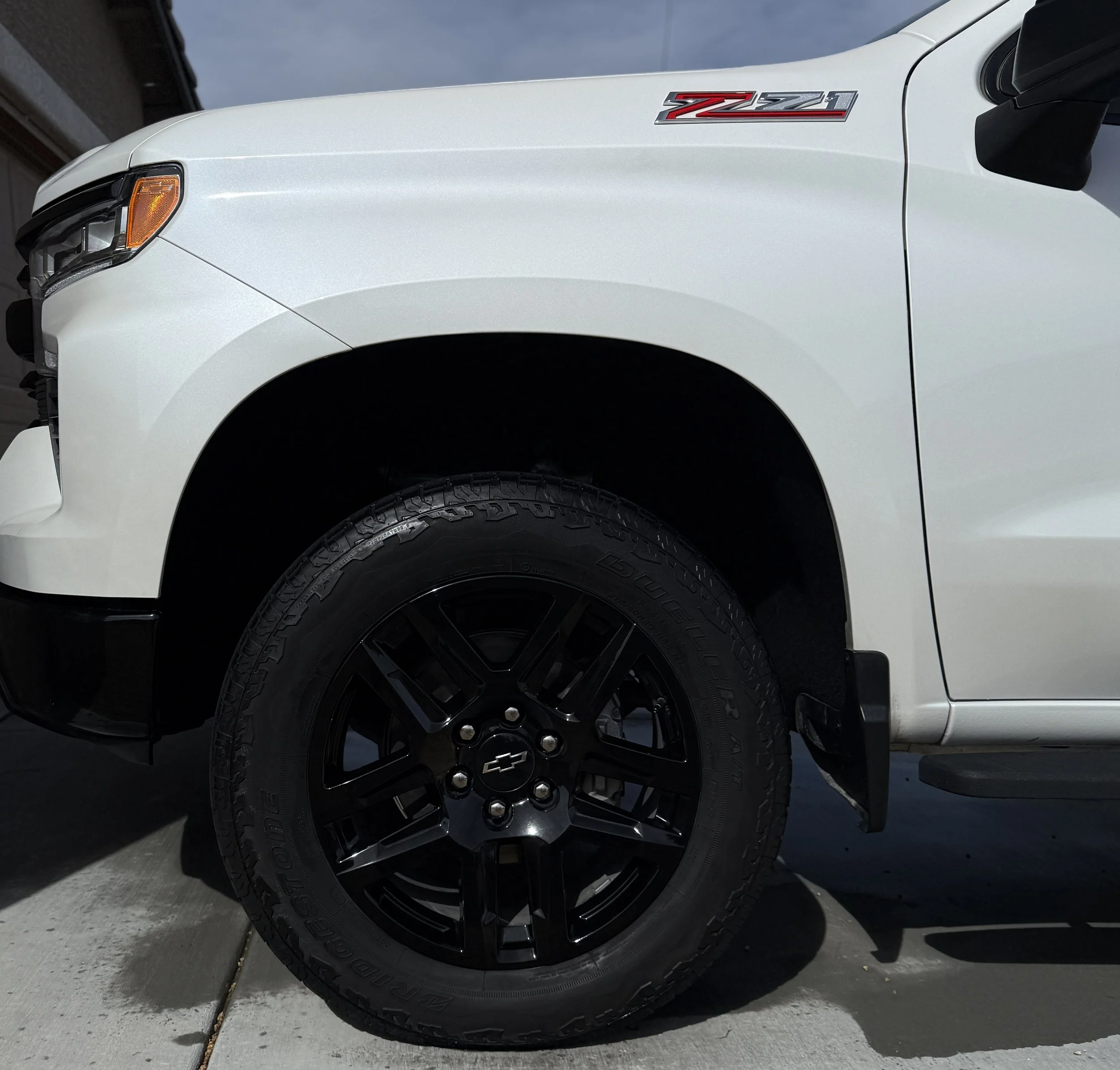 Close-up of the front left side of a white Chevrolet Silverado Z71 pickup truck, showing the black wheel and tire, and Z71 badge on the fender.