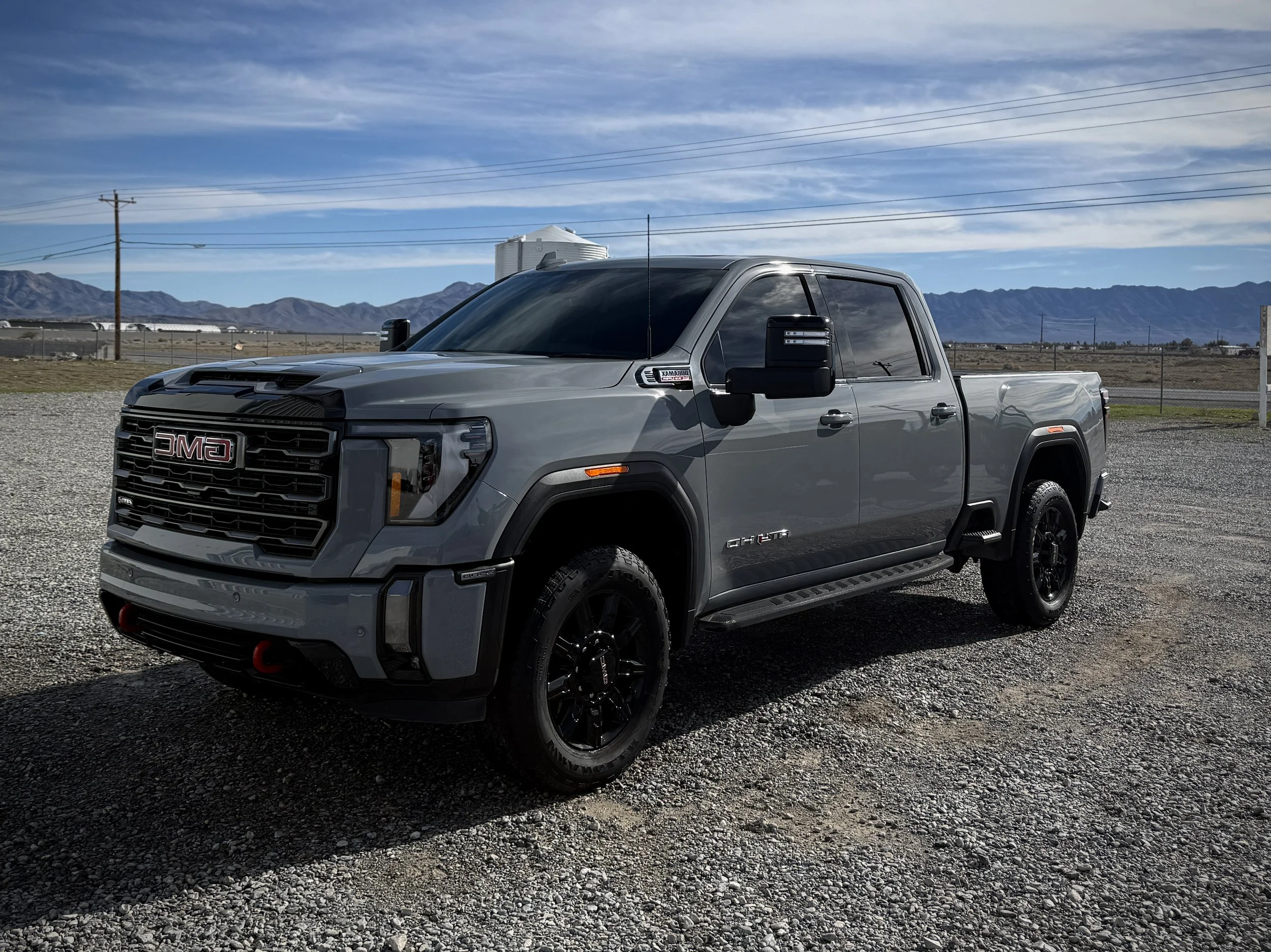 Gray GMC pickup truck parked on gravel lot with mountains and blue sky in background.