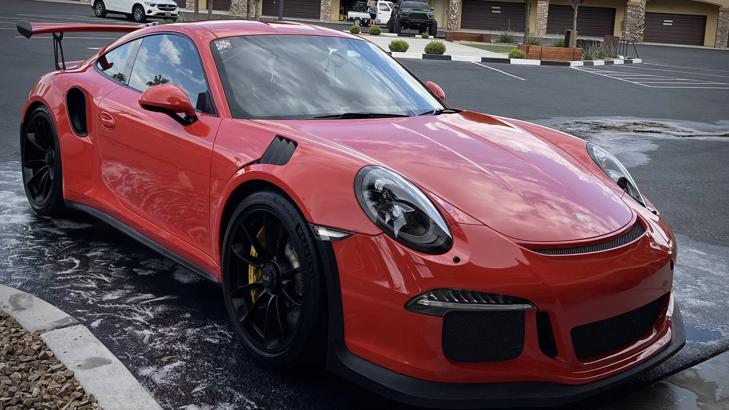 Red Porsche 911 sports car with black wheels and rear wing parked on a car wash mat