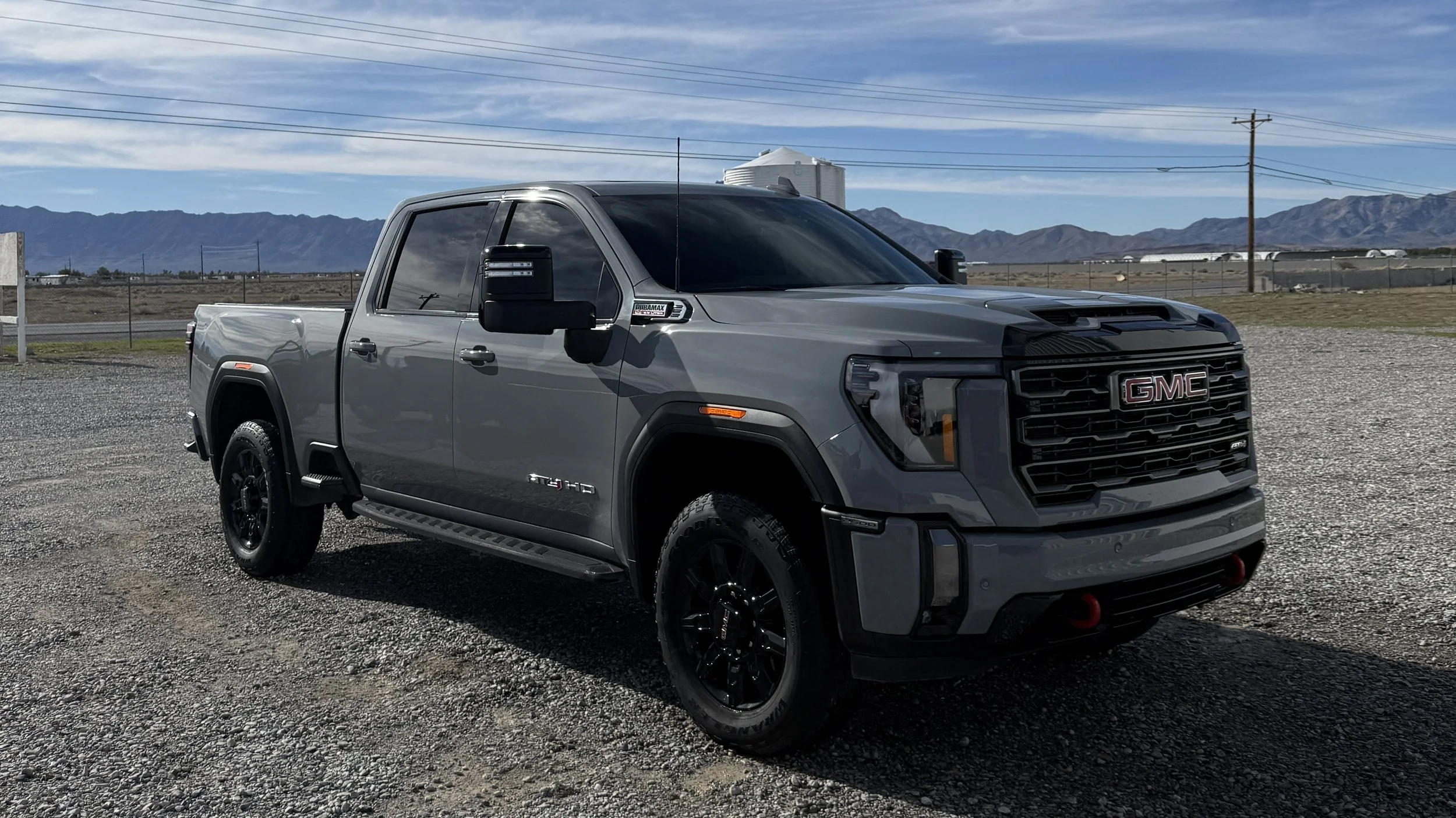 Gray GMC pickup truck parked on gravel, with mountains and blue sky in the background.