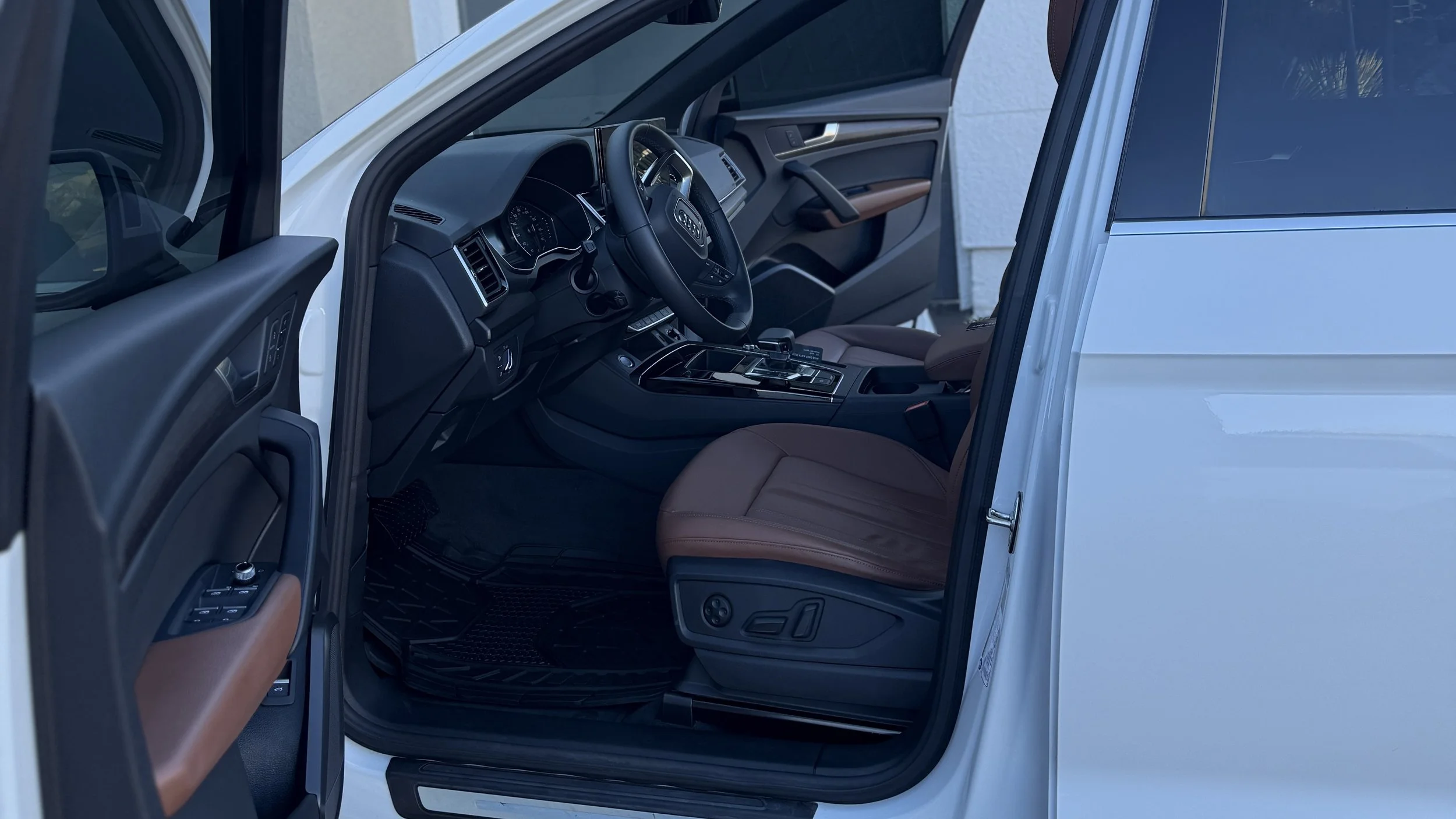 Interior of a white car showing the driver's seat, steering wheel, dashboard, and part of the front passenger seat with brown leather upholstery.