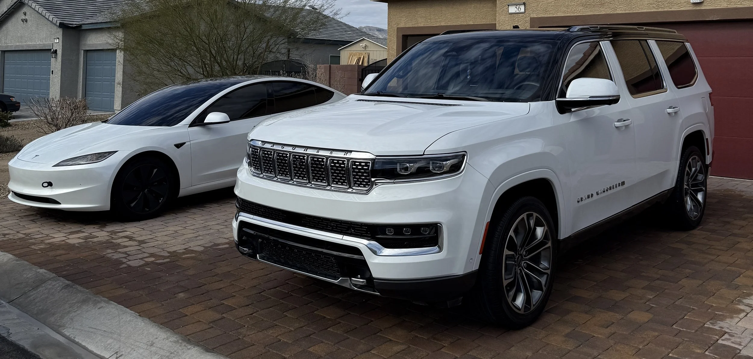 A white Tesla Model S parked next to a white Jeep Grand Wagoneer in a residential driveway.