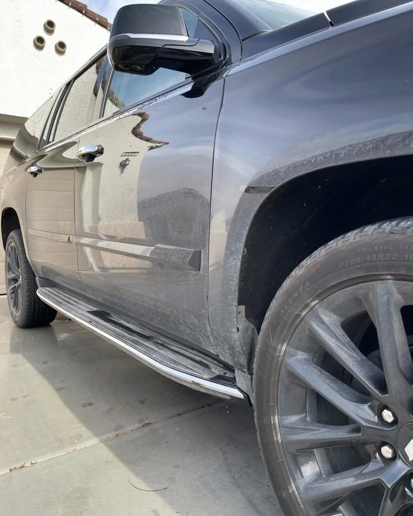 Black pickup truck with chrome side mirrors, large tires, and running boards, parked on a driveway in front of a house.