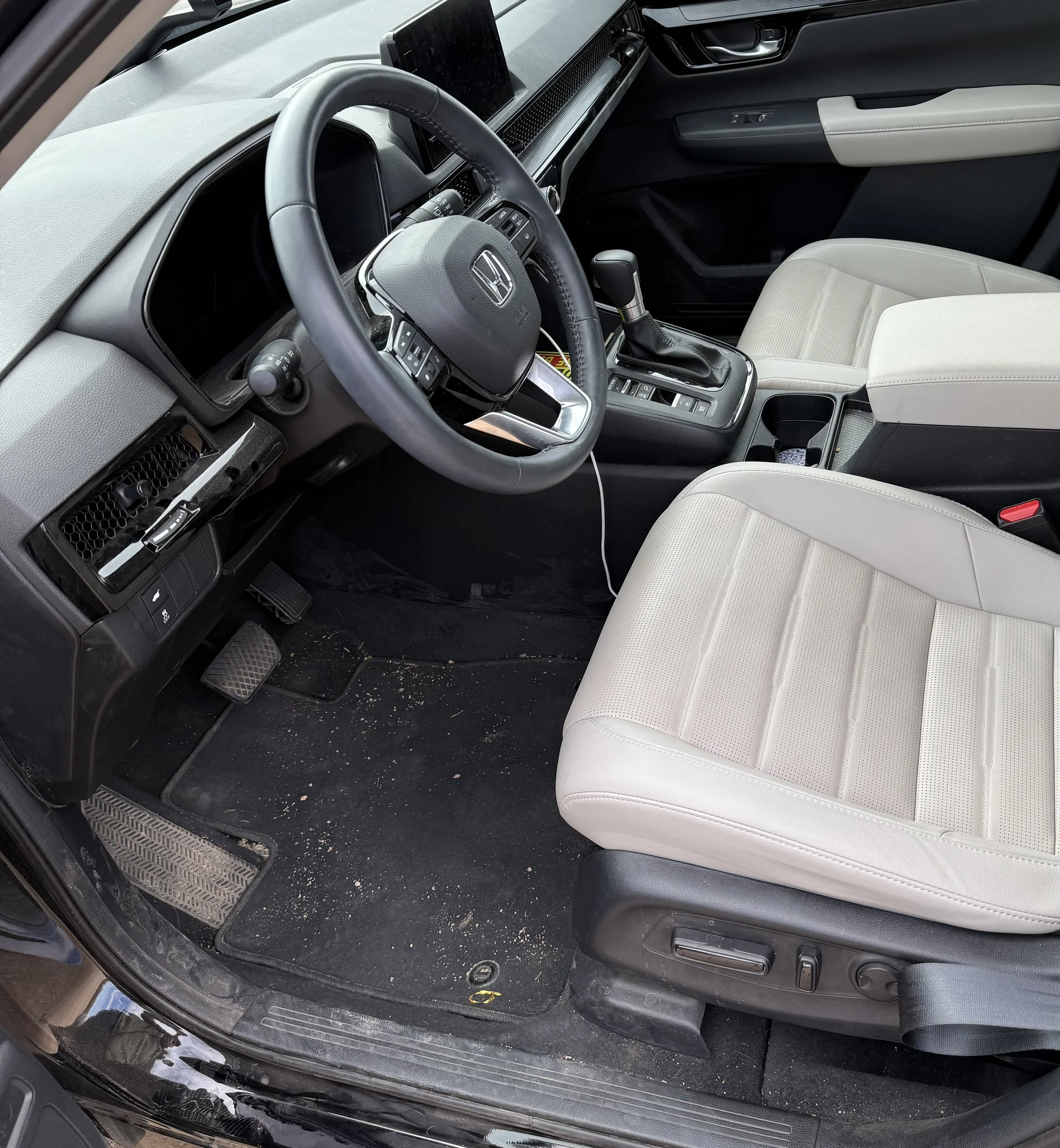 Interior of a Honda vehicle showing the driver's seat, steering wheel, gear shifter, and front passenger seat with some dirt on the floor.