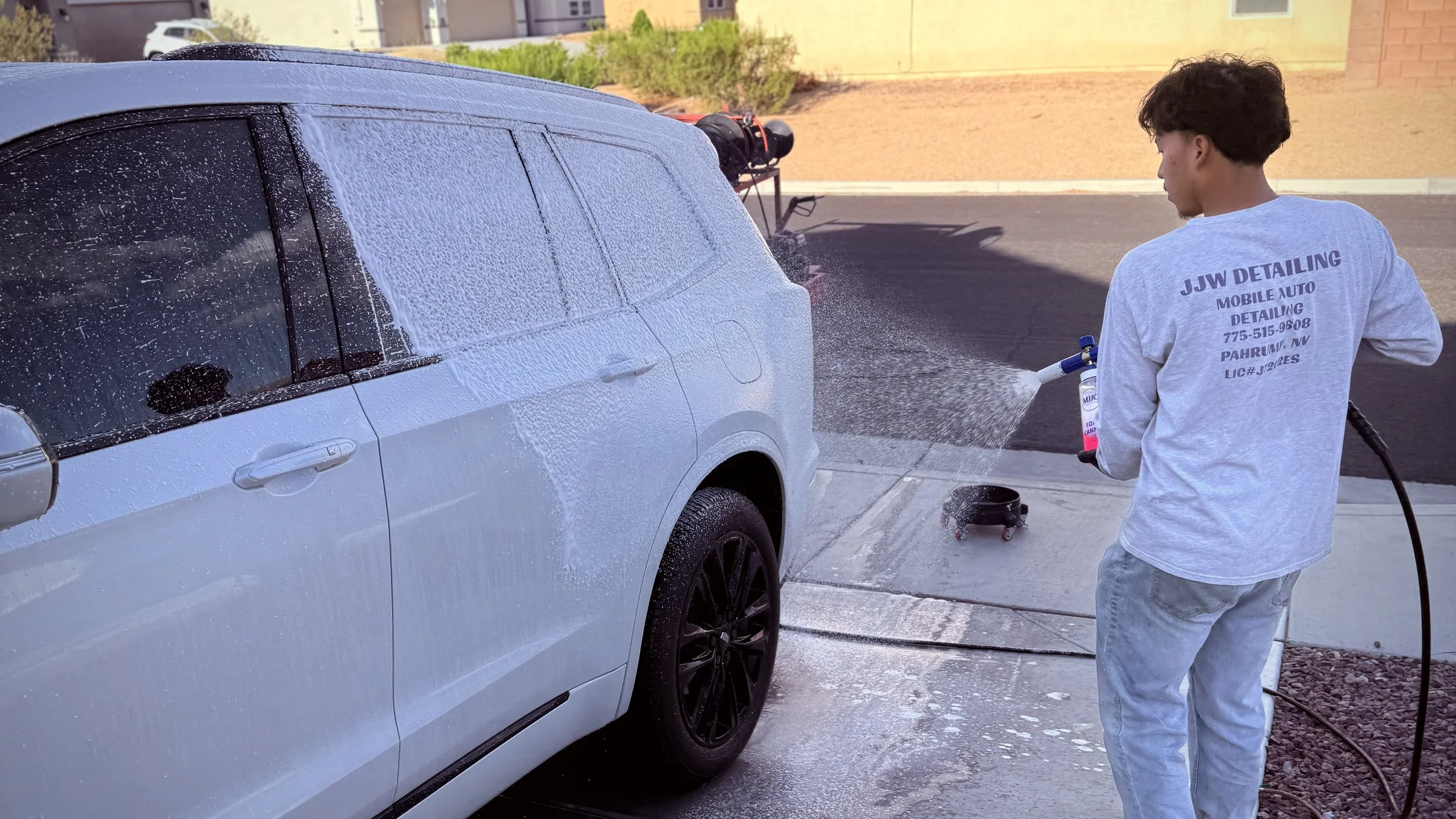 A person washing a white SUV with foam using a power washer outside on a paved driveway.