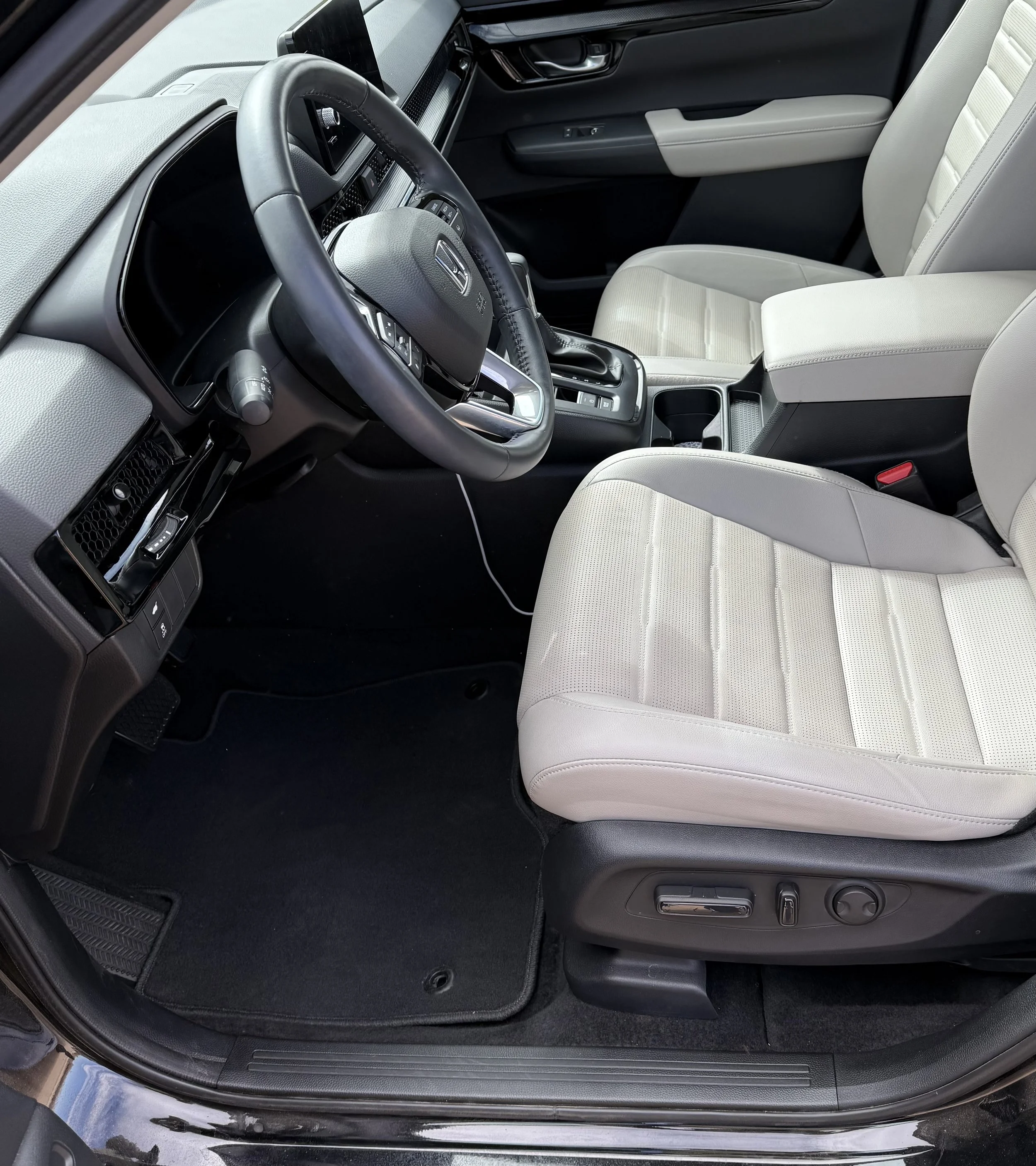 Inside view of a vehicle showing the driver's seat, steering wheel, dashboard, and front passenger seat with light-colored upholstery.