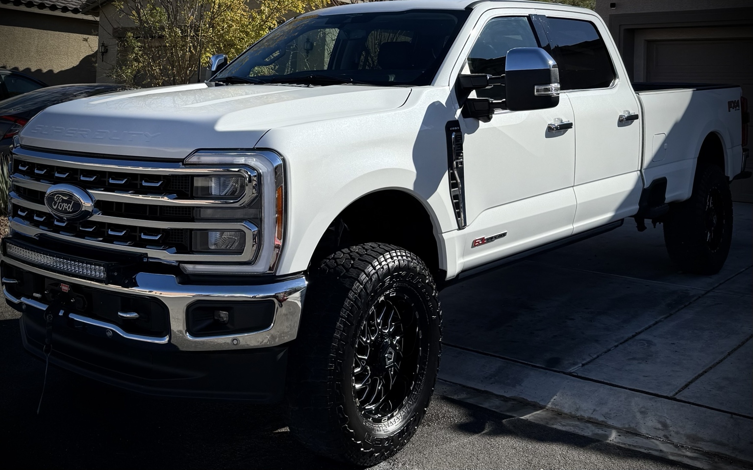White Ford Super Duty pickup truck parked on driveway with trees in background