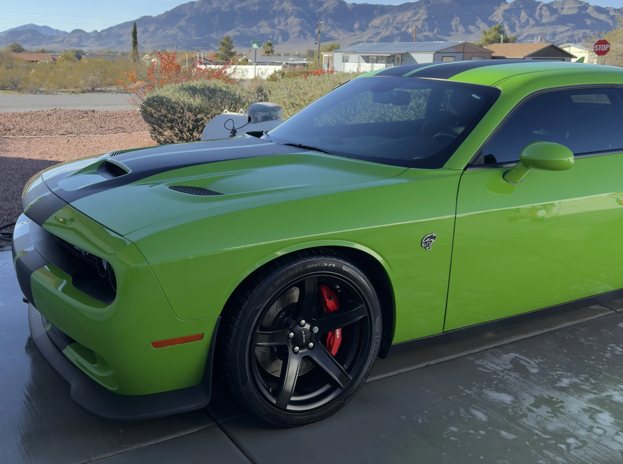 A bright green Dodge Challenger parked on a driveway with mountains and houses in the background.
