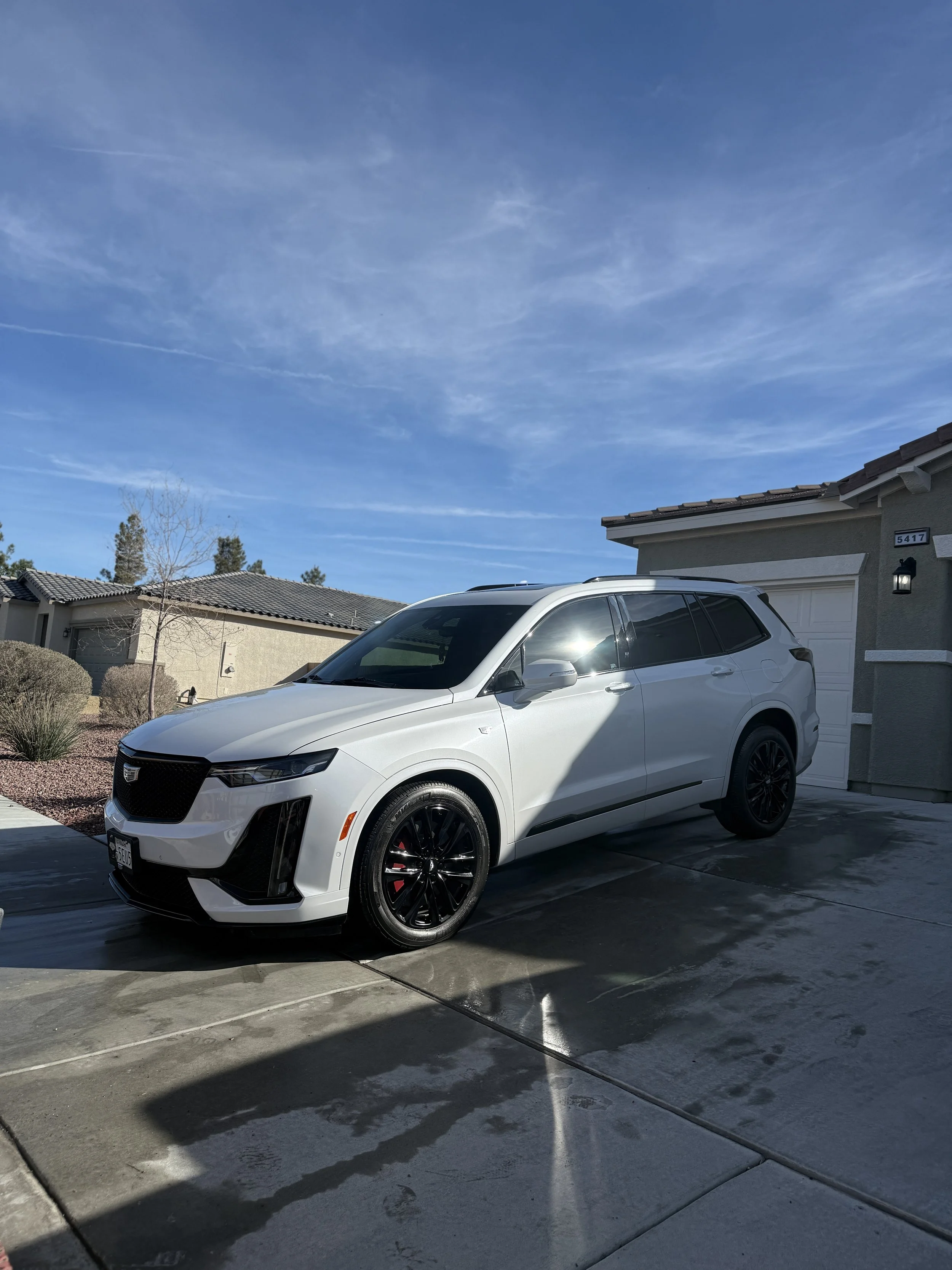 A white Cadillac SUV parked in a residential driveway on a sunny day, with clear blue sky and neighboring houses visible.