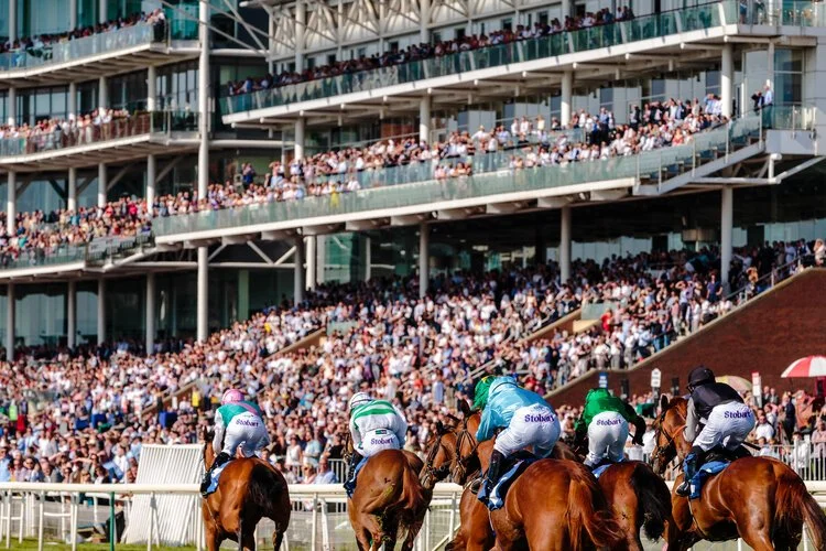 Horses and jockeys racing on a track at a large stadium filled with spectators.