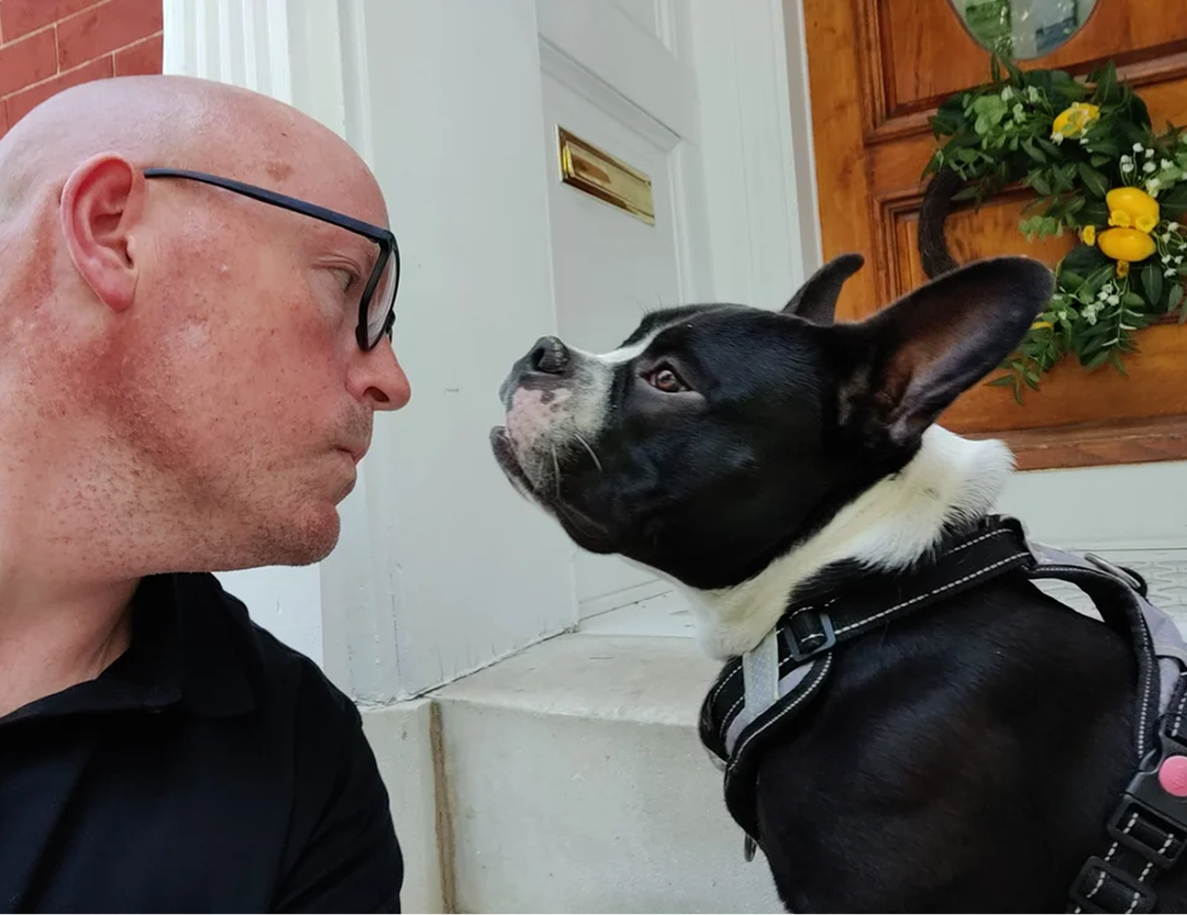 Scott Schultz and his Boston Terrier facing each other on front porch steps, close up.
