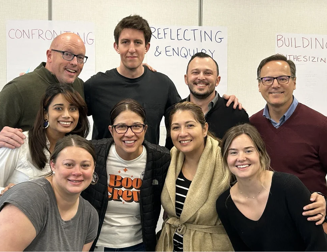 Scott Schultz with a cohort group of five women and four men, gathered together in an indoor setting.