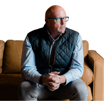 Scott Schultz sitting on a sofa looking to the side.