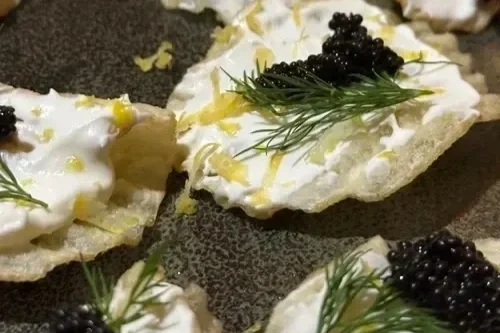Close-up of open-faced appetizers with creamy spread, black caviar, fresh dill, and lemon zest on bread slices.