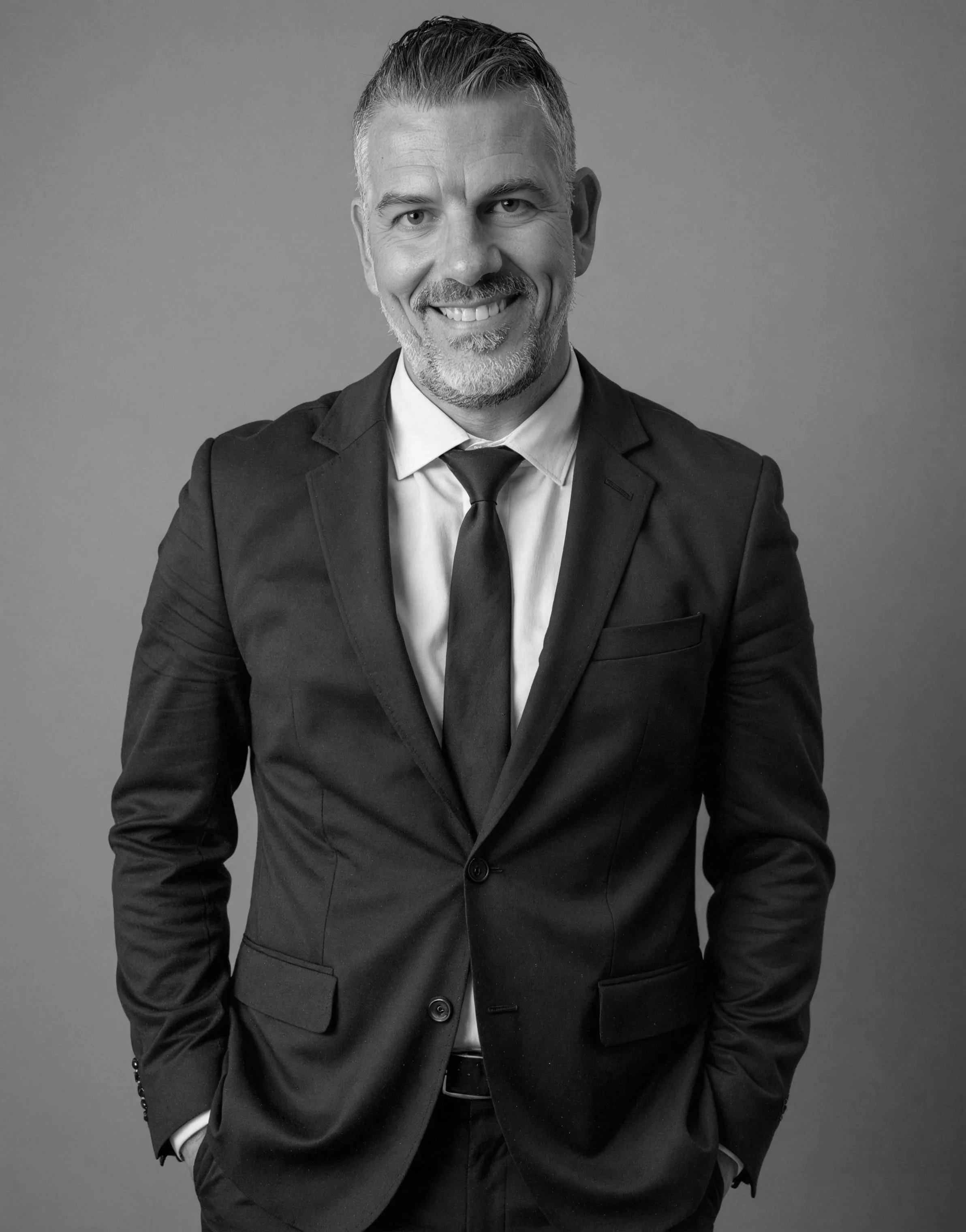 Smiling man in a suit and white shirt in an office setting.