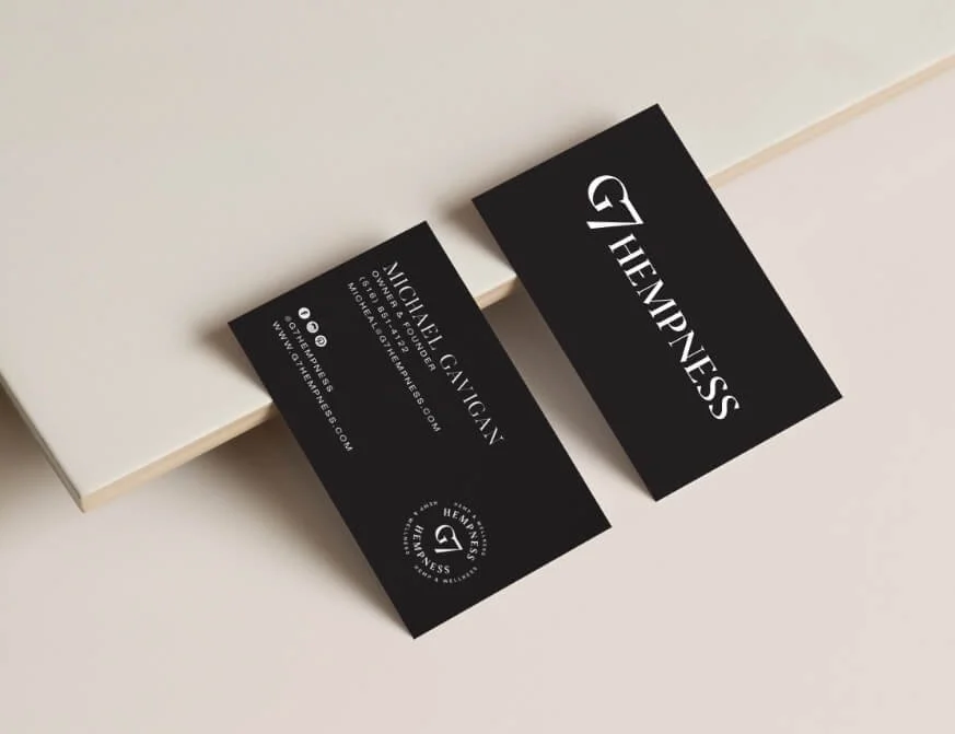 Black business cards for GHempeness with white text, placed on a light surface. One card displays the name GHempeness, and the other has contact information for Alicia Lavagna, a business owner.