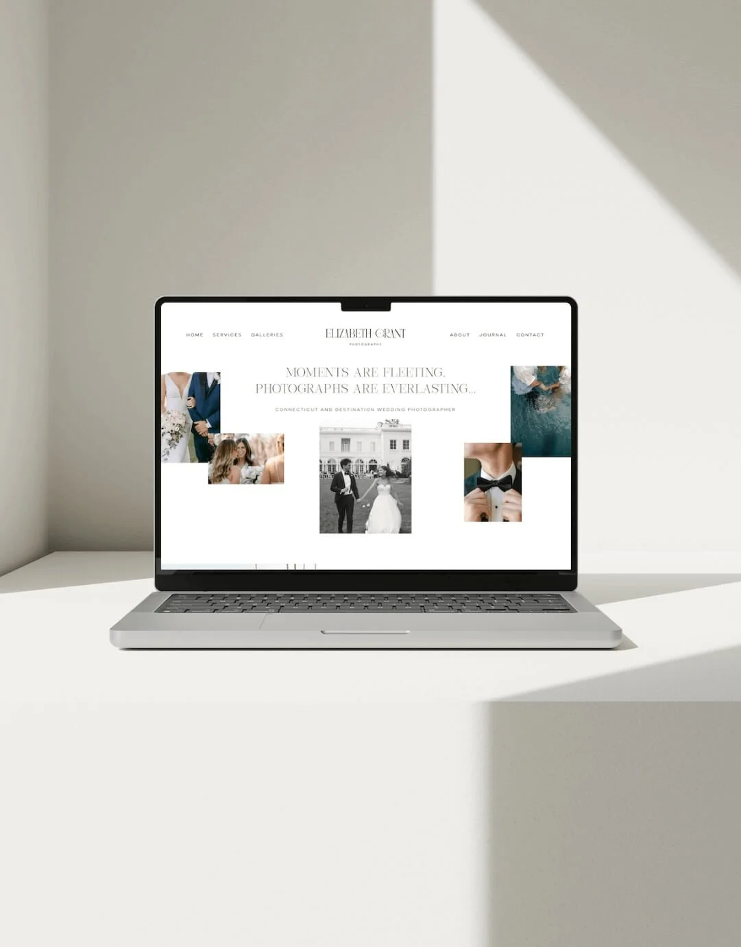 Open laptop displaying a wedding photography website on a white table in a minimalist setting.