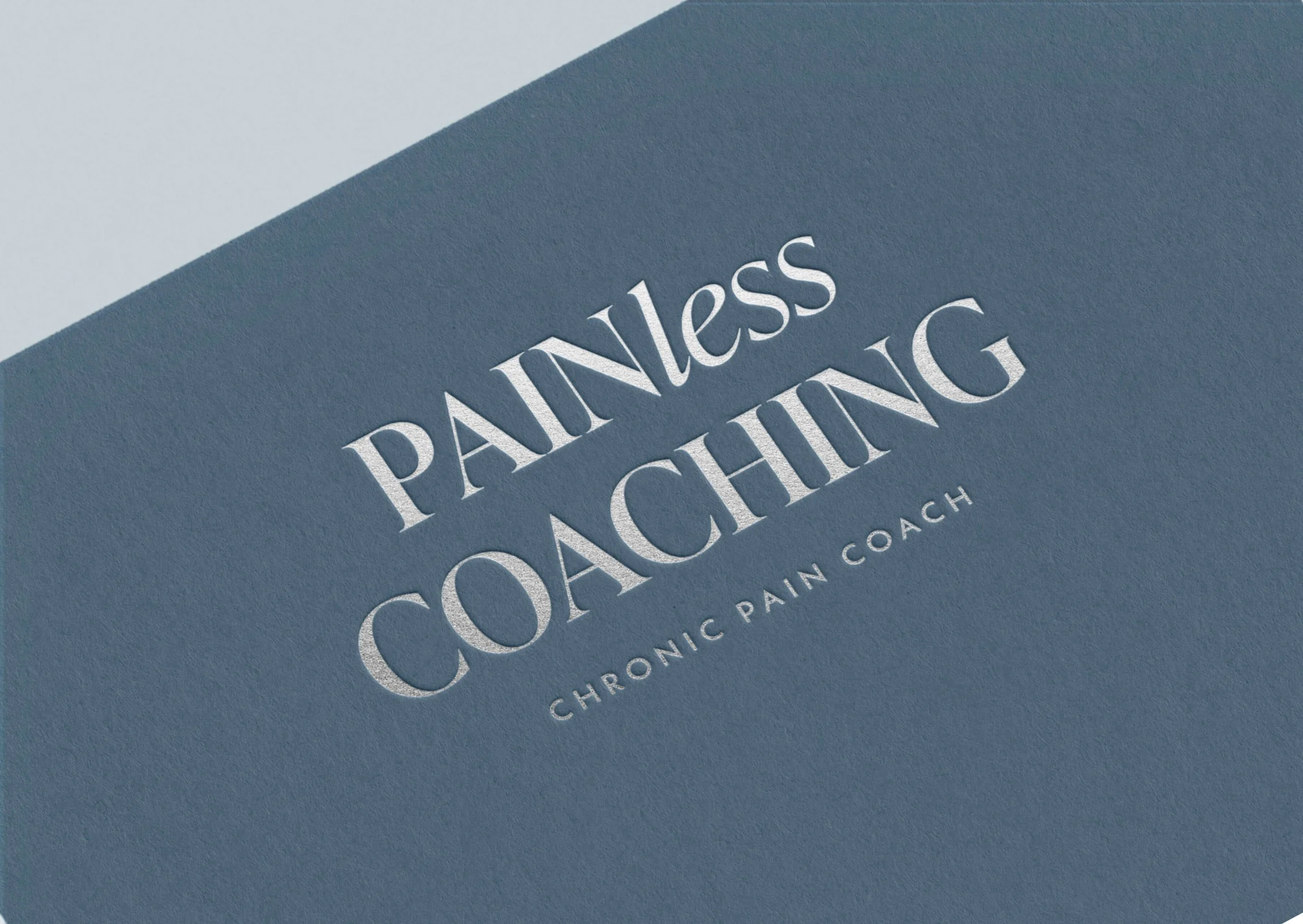 Blue textured paper or card with embossed silver text that reads "PainLess Coaching" and smaller text below that says "Chronic Pain Coach."