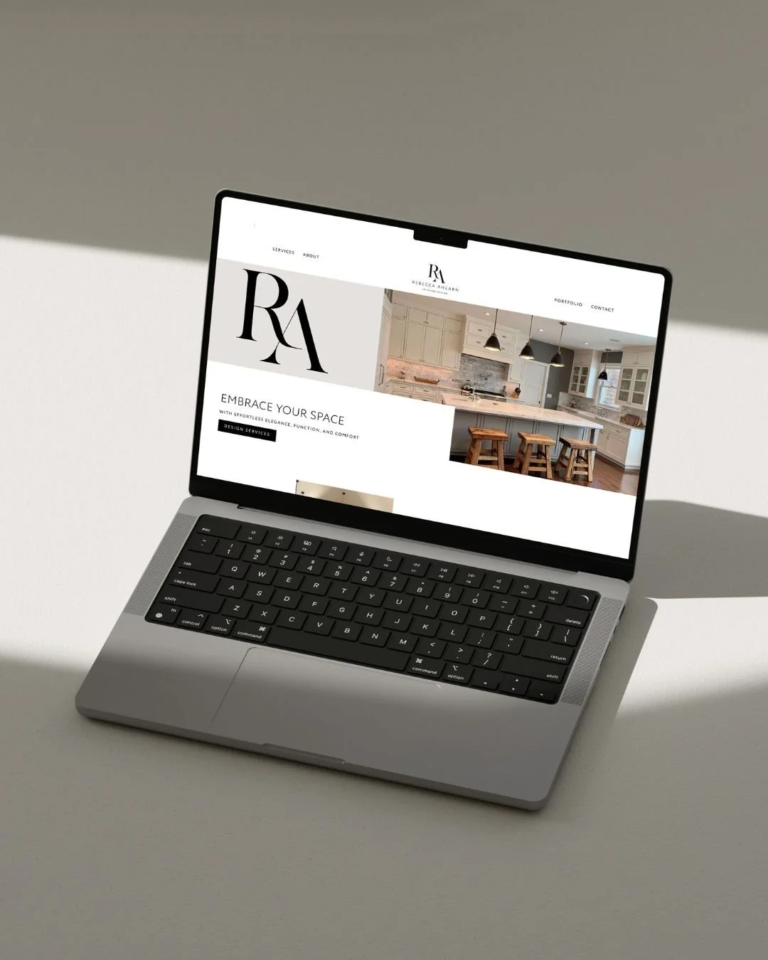 Laptop displaying a website for Rebecca McCarran, featuring a kitchen with white cabinets, a marble tile backsplash, and a kitchen island with barstools.