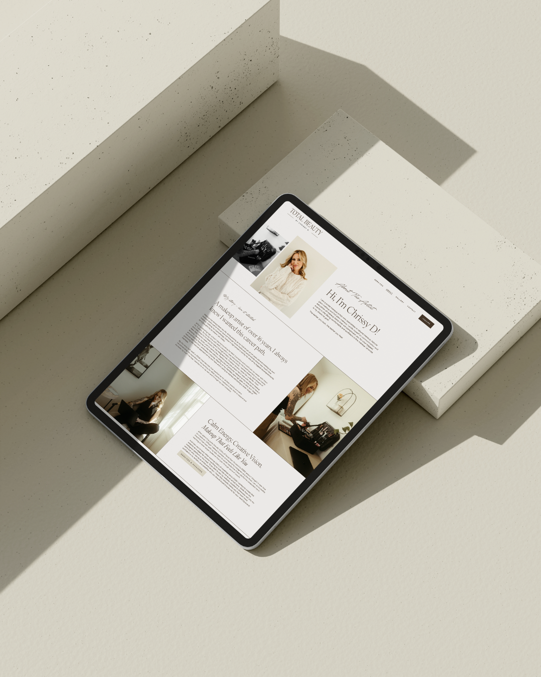 Tablet displaying a personal website on a white textured surface with geometric blocks in the background.