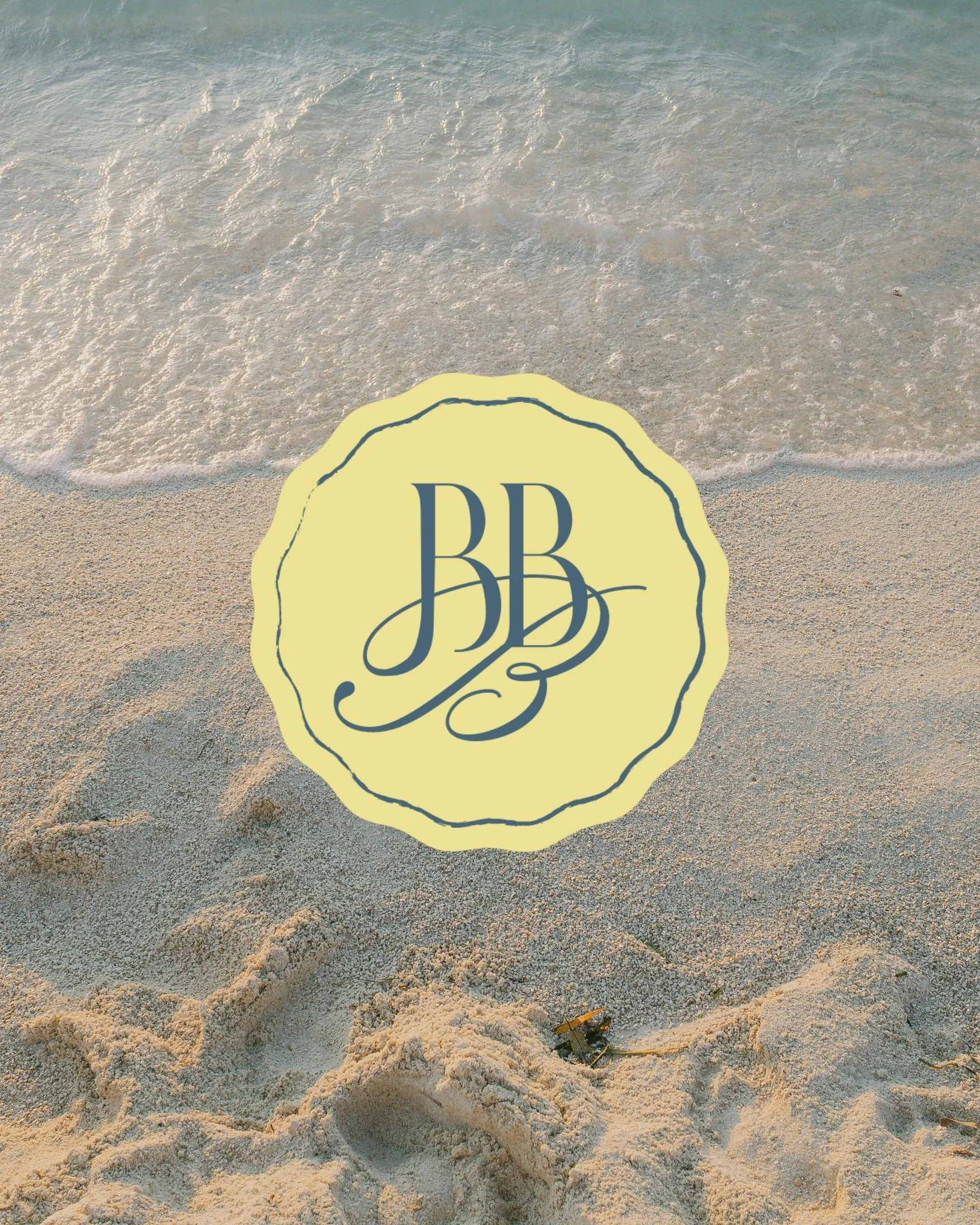 Beach with sand and gentle waves, a yellow logo with the initials 'JBB' in cursive is placed on the sand.