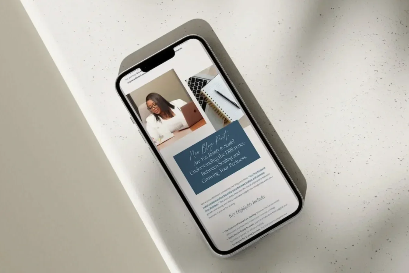 Smartphone on a white table displaying a webpage about understanding scaling and growing a business, with a photo of a woman wearing glasses and working on a laptop.