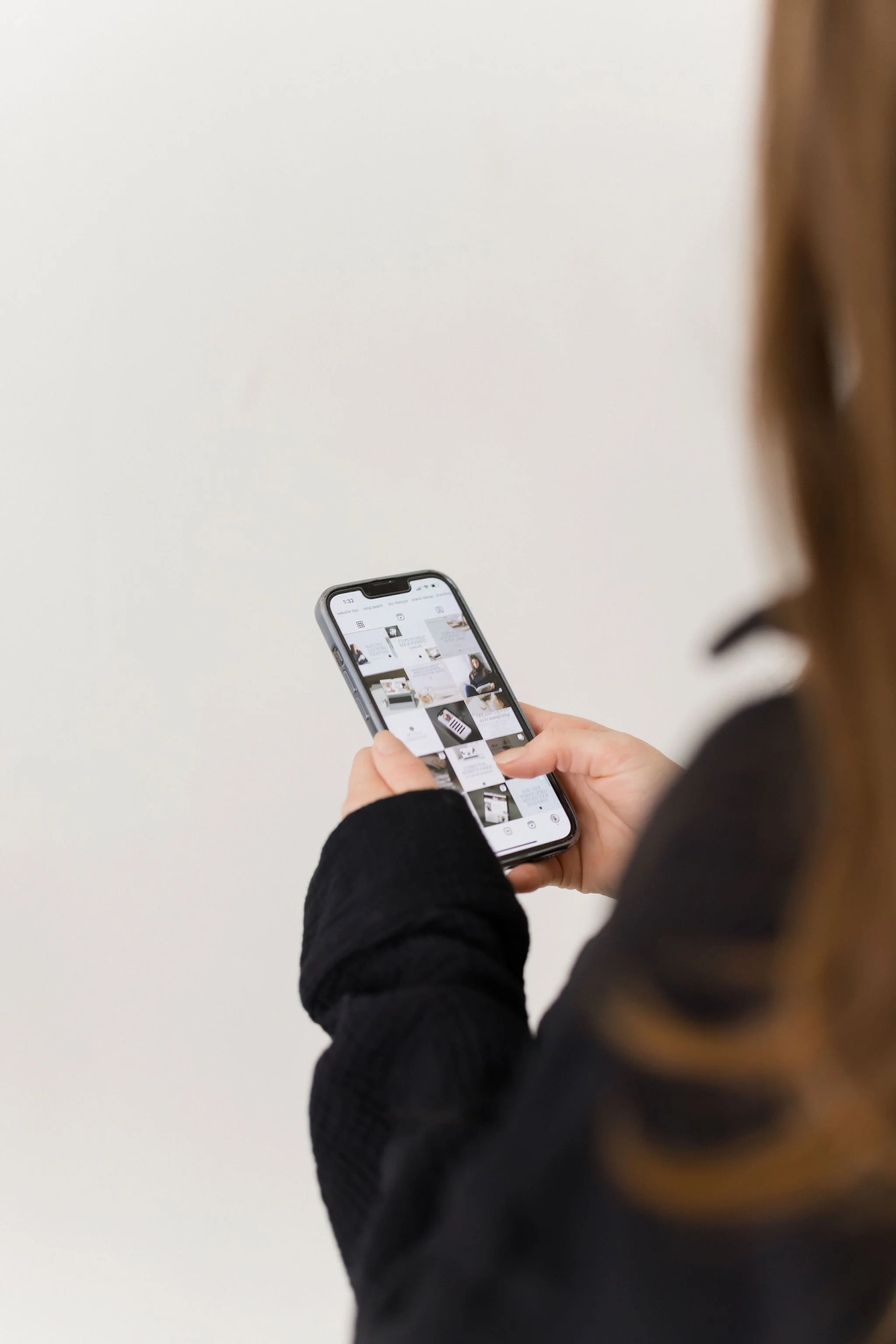 Person using a smartphone to browse images, with a plain white wall in the background.