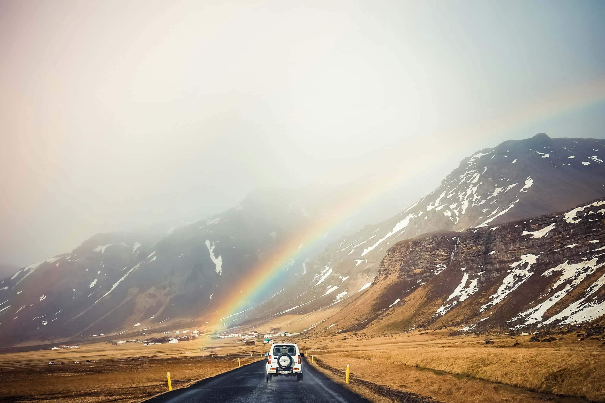 SUV driving through the mountains under a rainbow