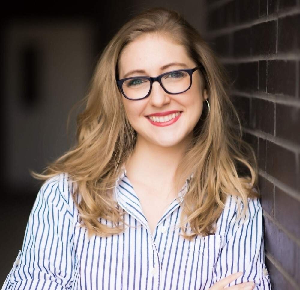 Headshot of a blonde woman with glasses in a blue striped shirt.