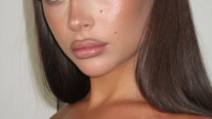 Close-up of a woman's face and shoulders, showing her brown hair, full lips, and clear skin.