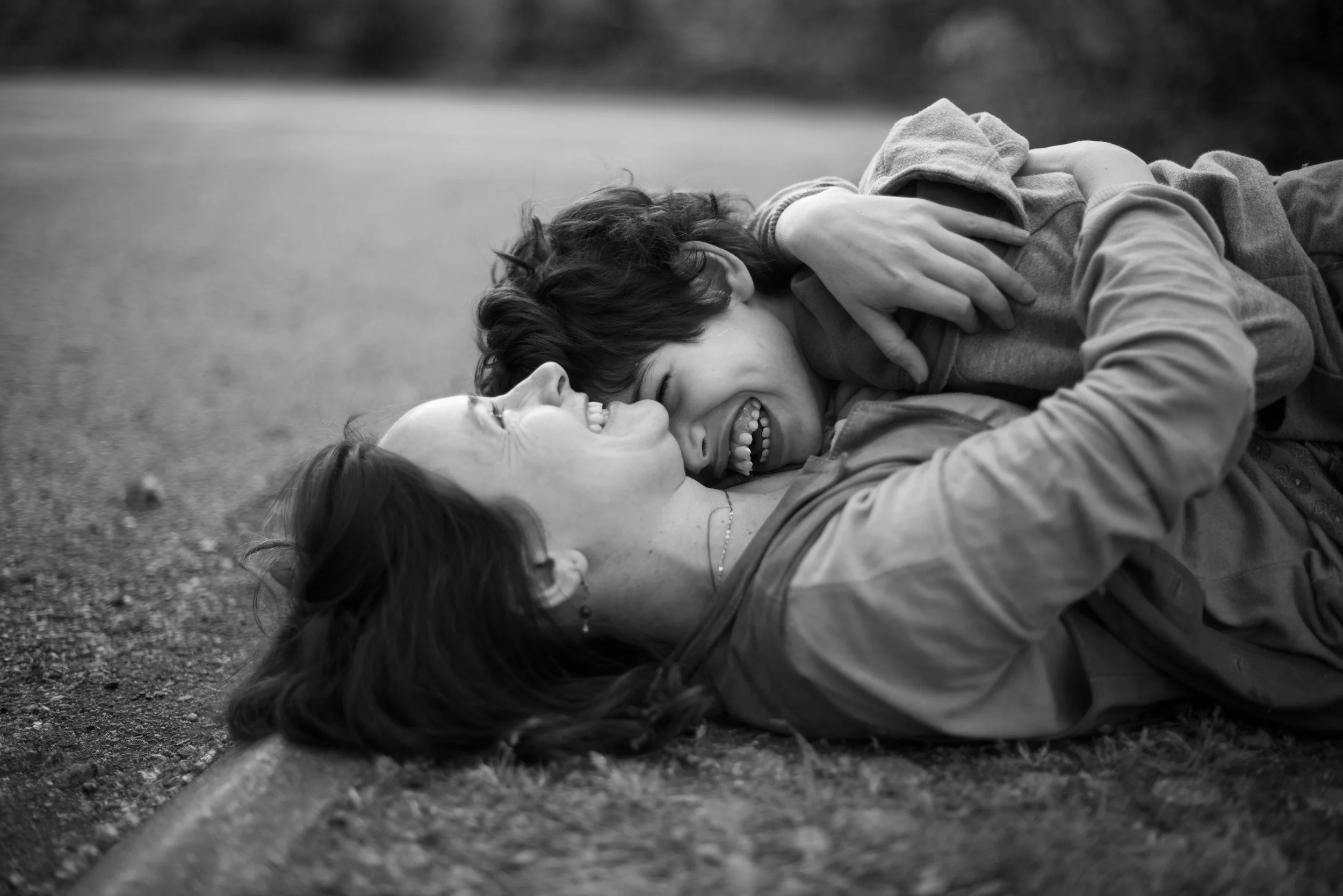 Mother and daughter outdoors, laughing and playfully interacting on the grass.