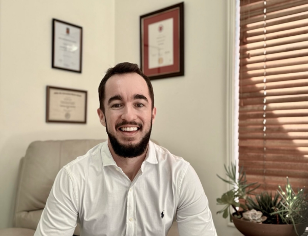 Smiling clinical counsellor sitting in an office, with professional diplomas and certificates on the wall.