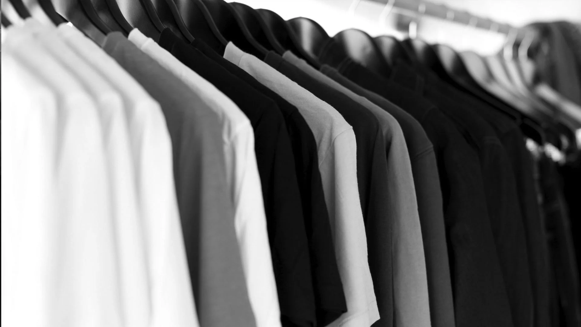 Clothing rack with white, gray, and black T-shirts hanging on black hangers.
