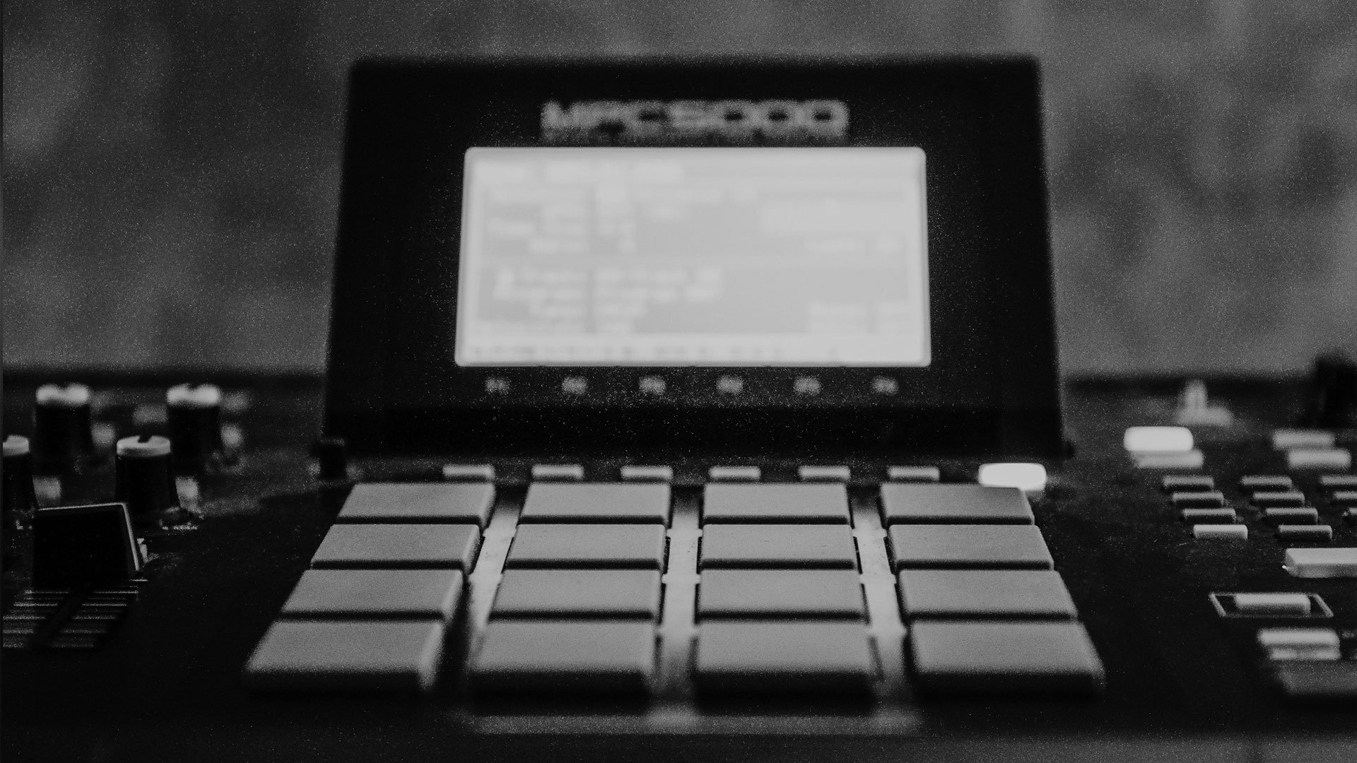 Close-up of a digital music production device with multiple large pads and control knobs, in black and white.