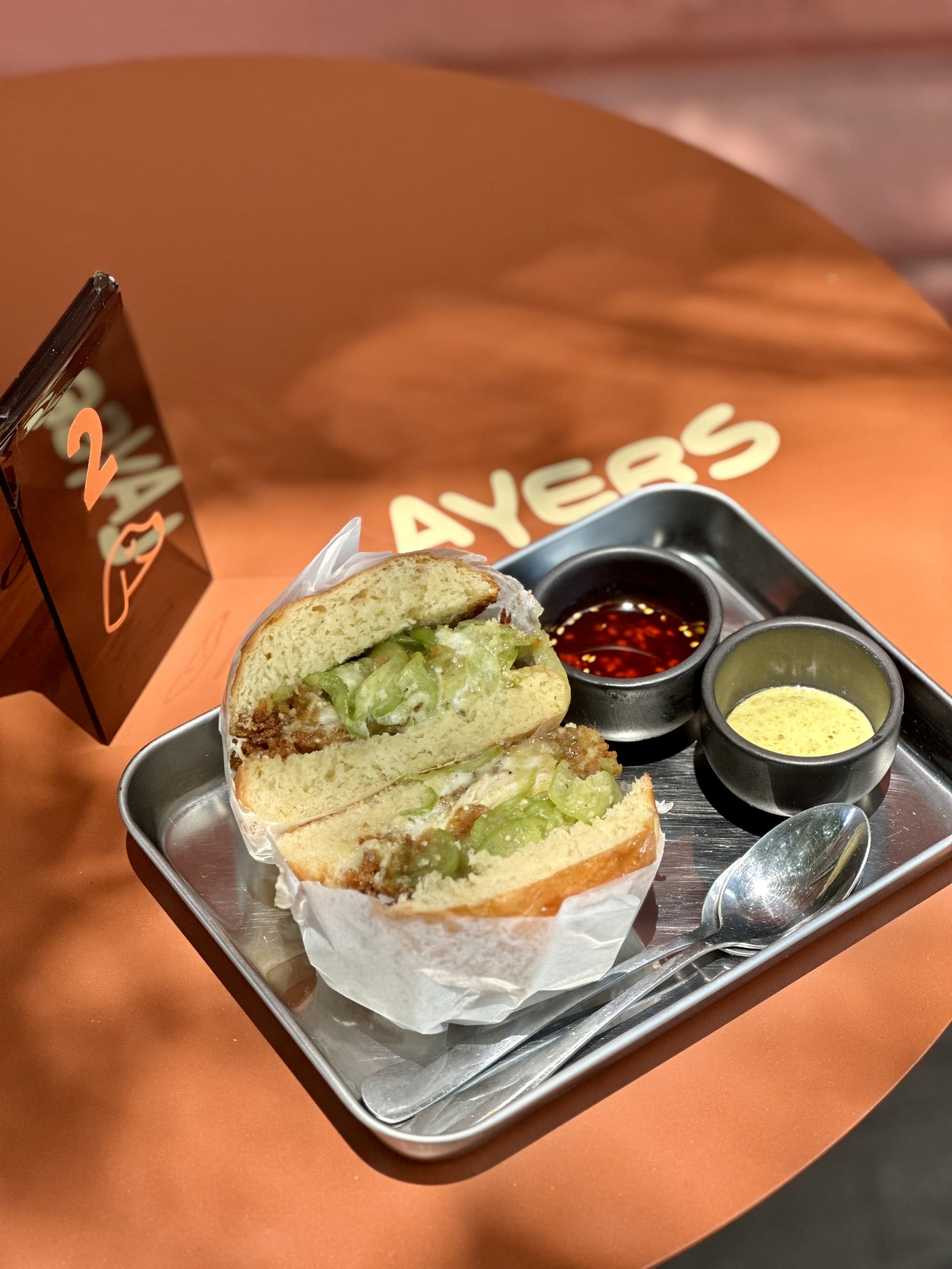 Sandwich de pan francés con carne, lechuga y jitomate, acompañado de salsas picantes y mostaza en un plato de metal.