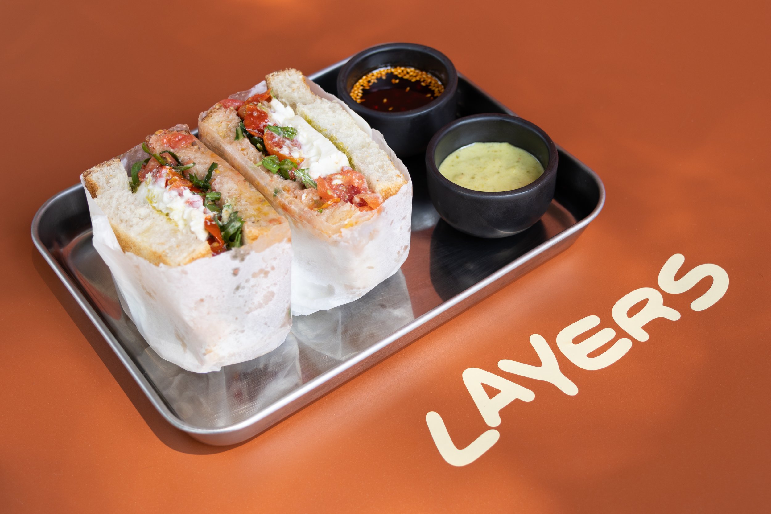 Burritos con verduras, acompañados de dos salsas en cuencos negros en una bandeja de metal, sobre una mesa anaranjada con la palabra 'LA VEGAS' escrita.