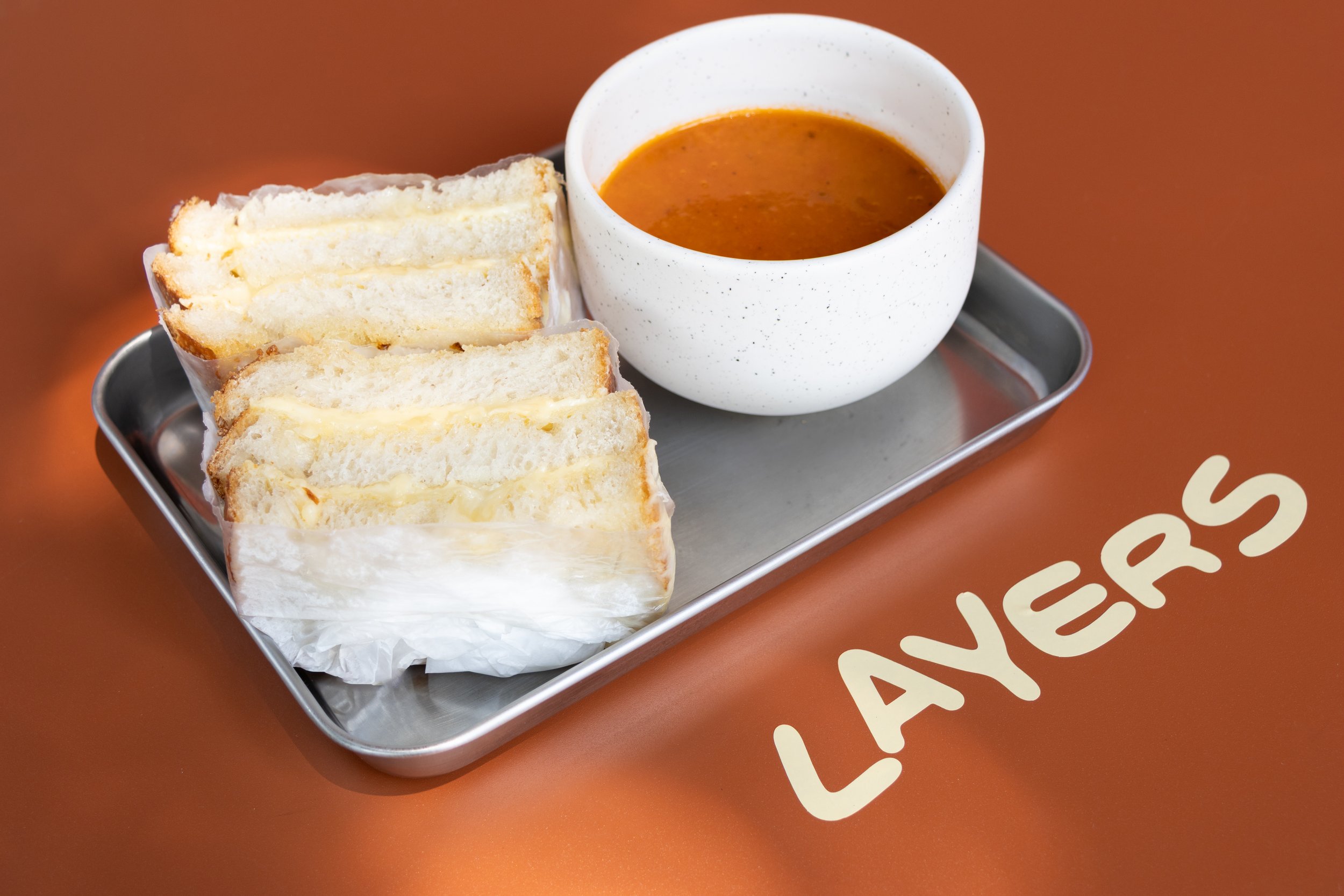 Sandwich de pan blanco con queso y sopa en taza blanca en bandeja de metal sobre mesa de color marrón