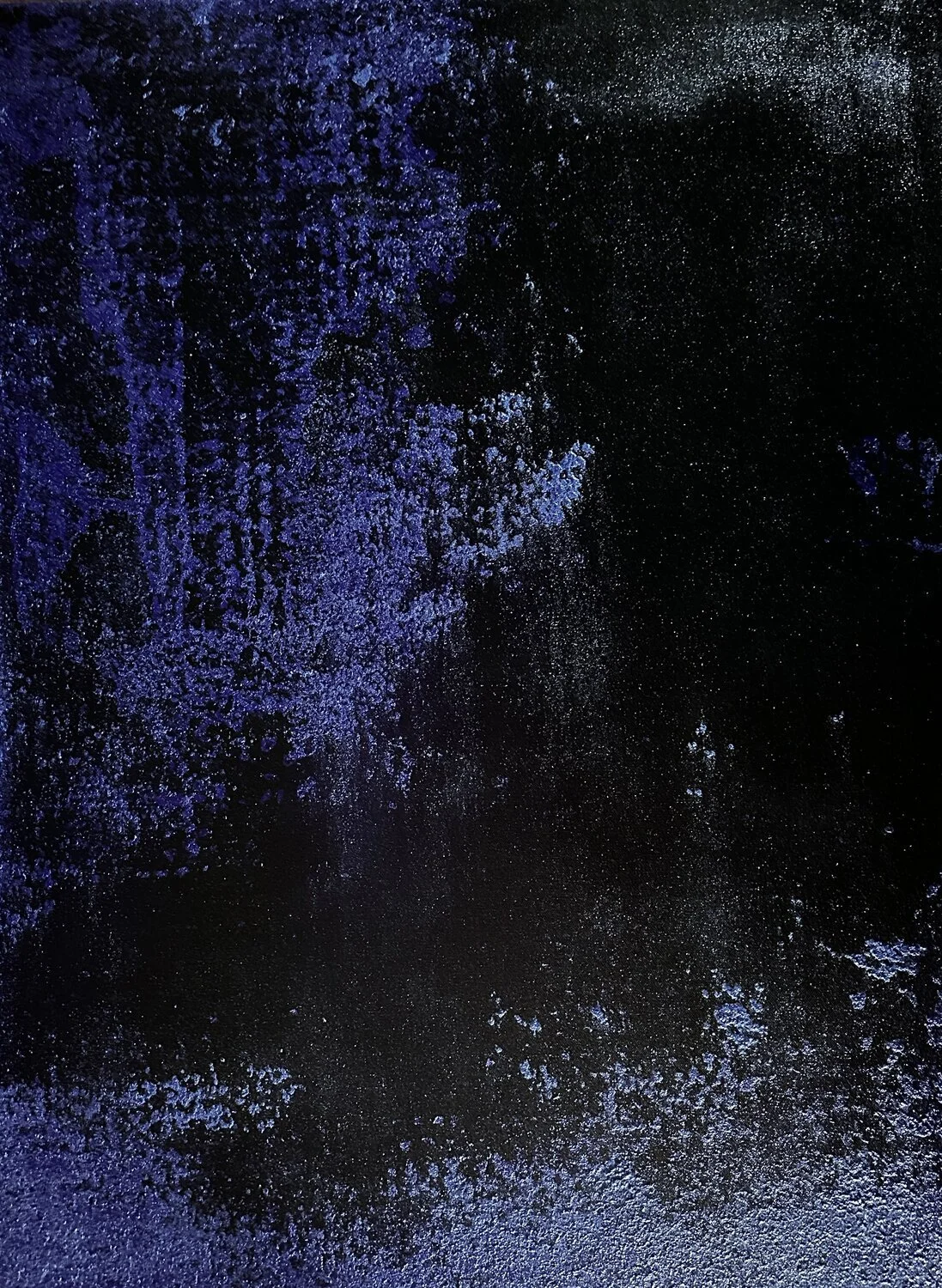 A black surface with blue and white specks and splashes of paint creating an abstract pattern.