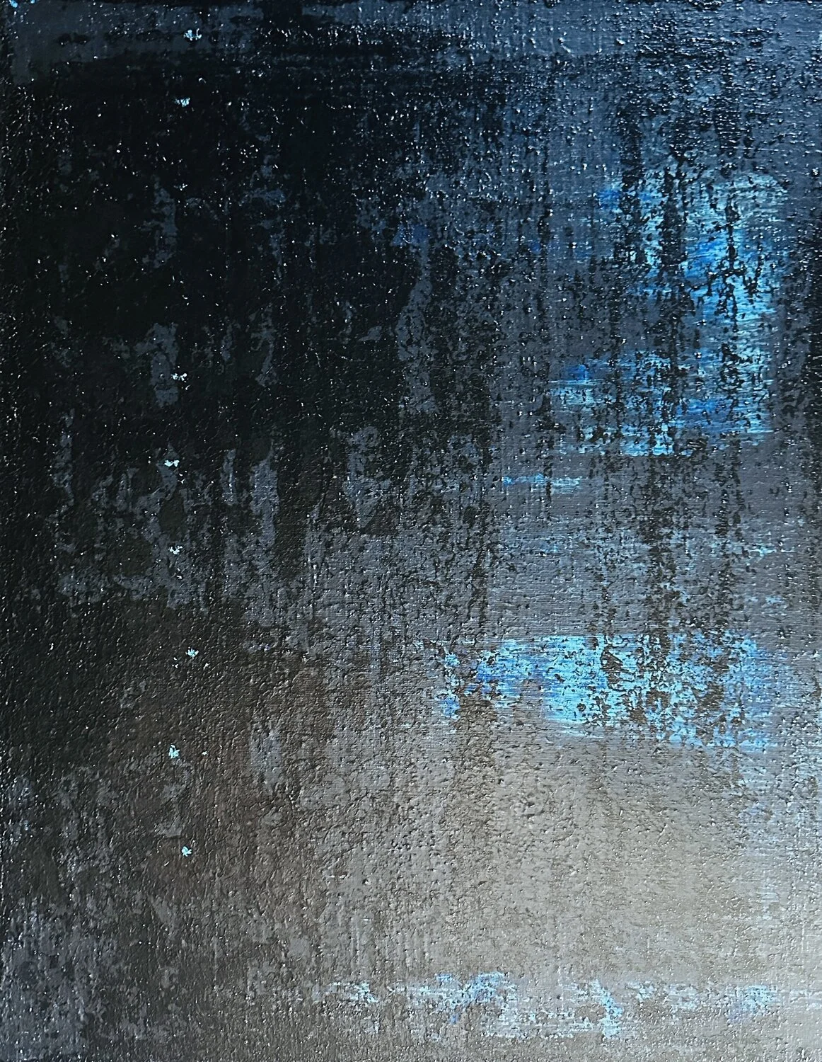 Close-up of a wet, textured, dark surface with patches of blue paint or light reflecting off it.