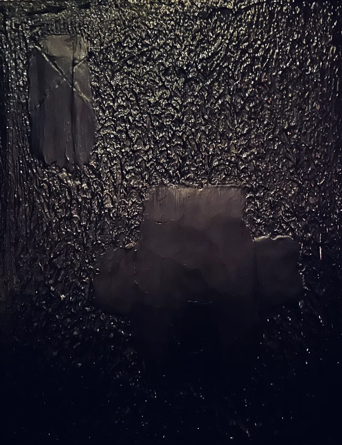 Close-up image of a black surface with textured, rough, and shiny appearance, featuring two smooth, shiny patches that look like scratches or cuts.