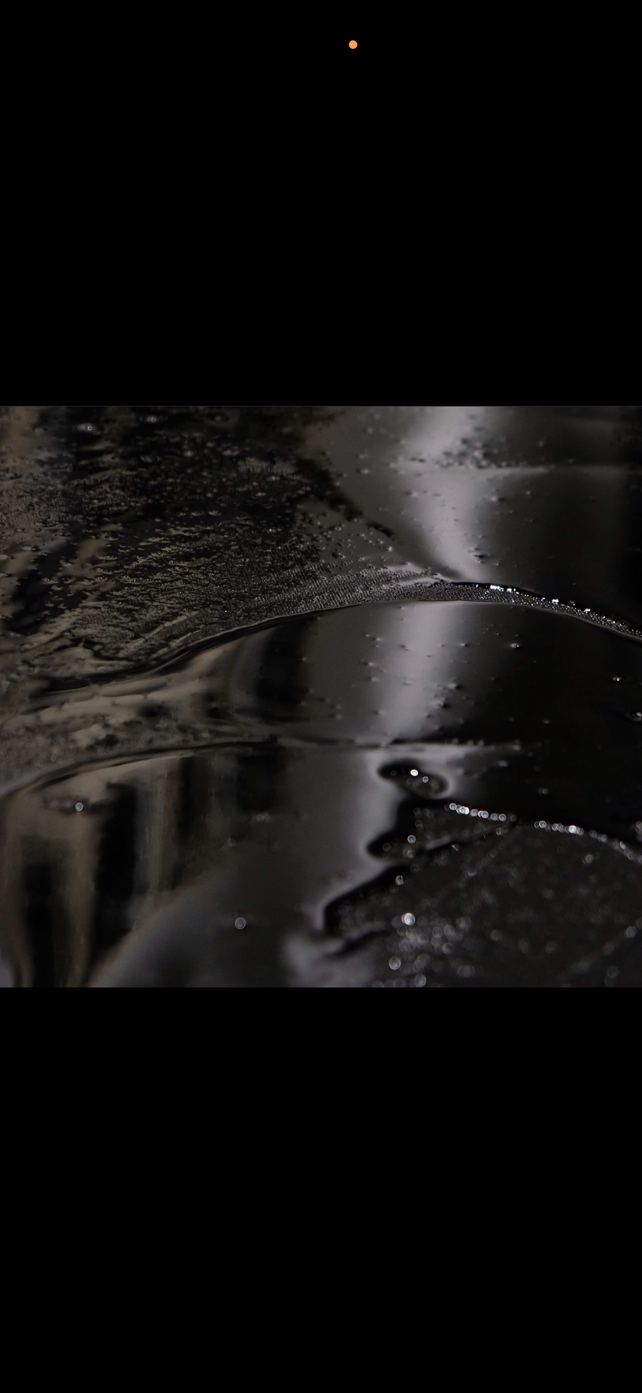 Close-up of a dark, reflective, wet surface with small water droplets and shiny spots.