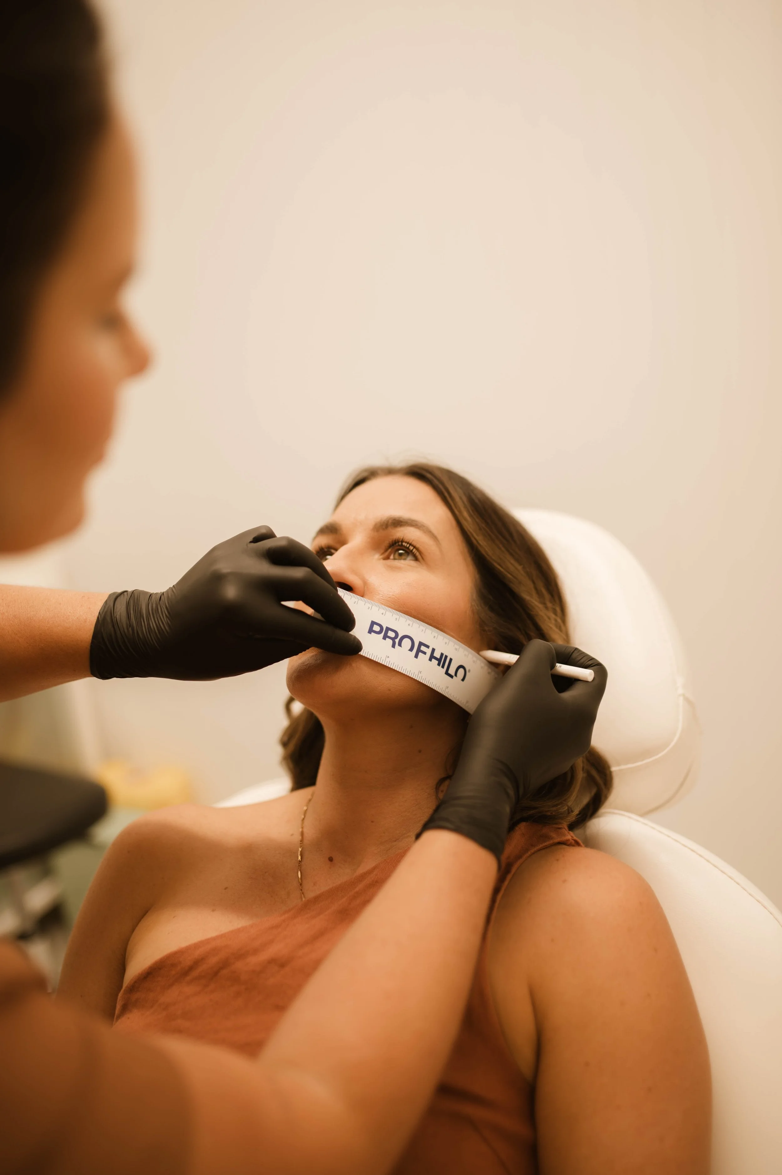 A woman receiving a facial measurement with a ruler held by a practitioner wearing black gloves.