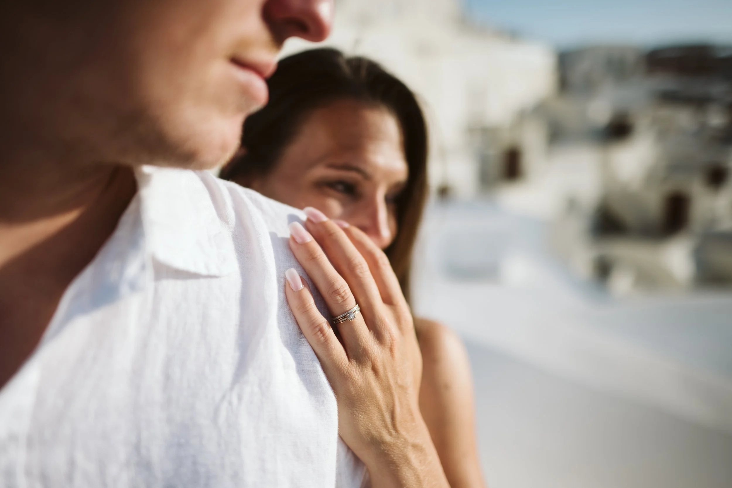 Close-up of a woman and a man with a blurred background of a beach or boardwalk.